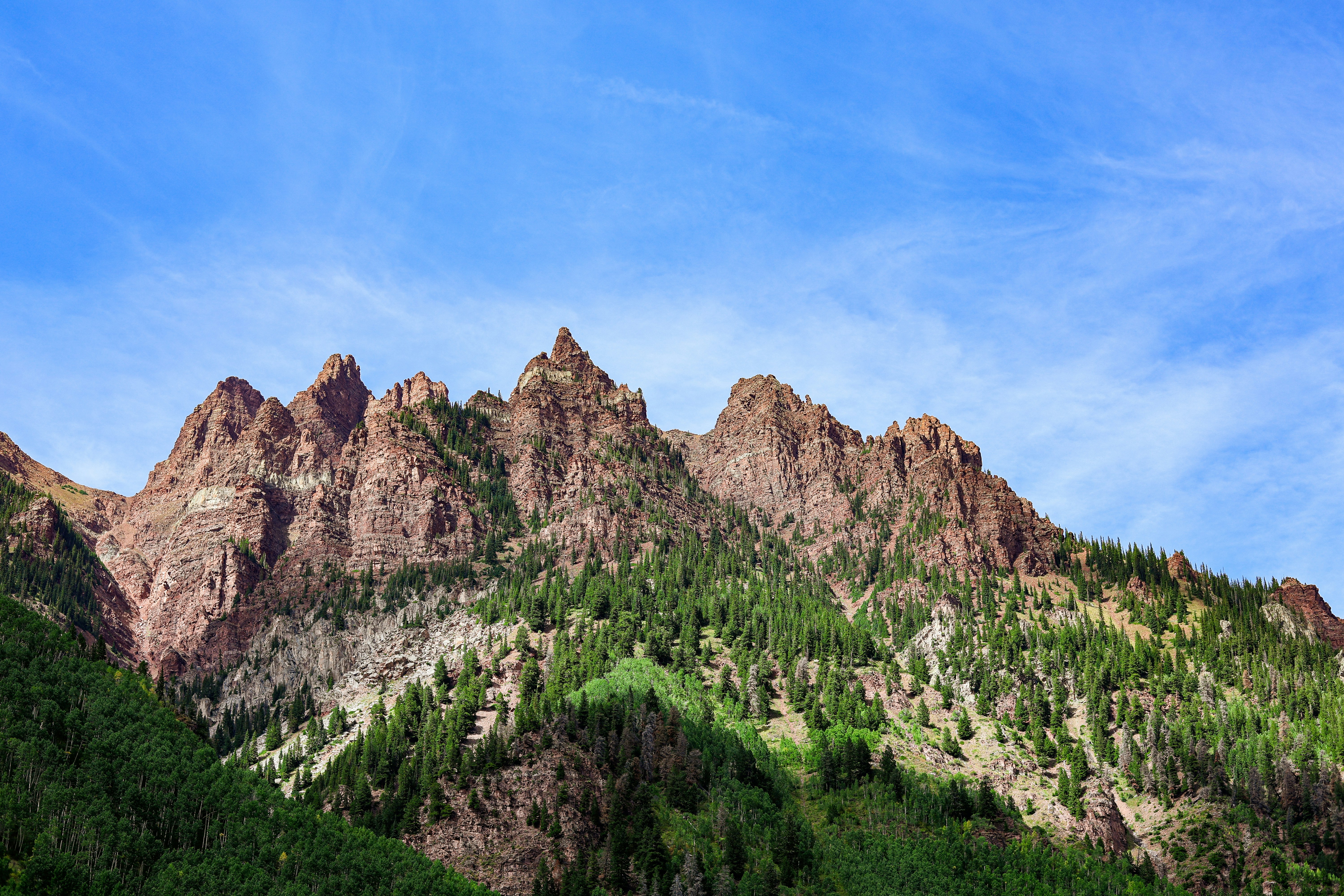 Cime montuose frastagliate ricoperte di alberi verdi sotto il cielo blu