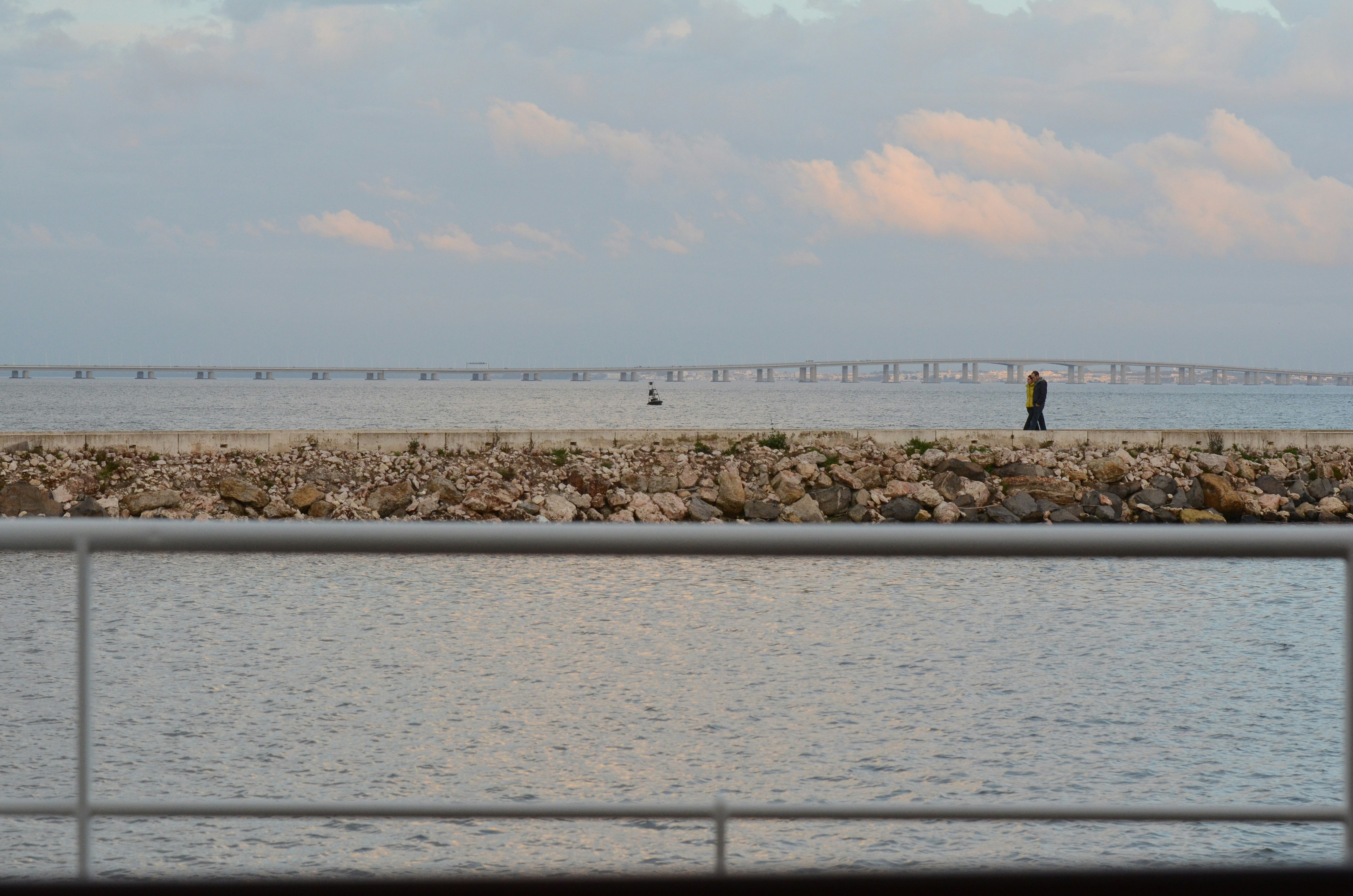 뒤에 다리가 있는 돌 부두 위를 걷는 사람들.