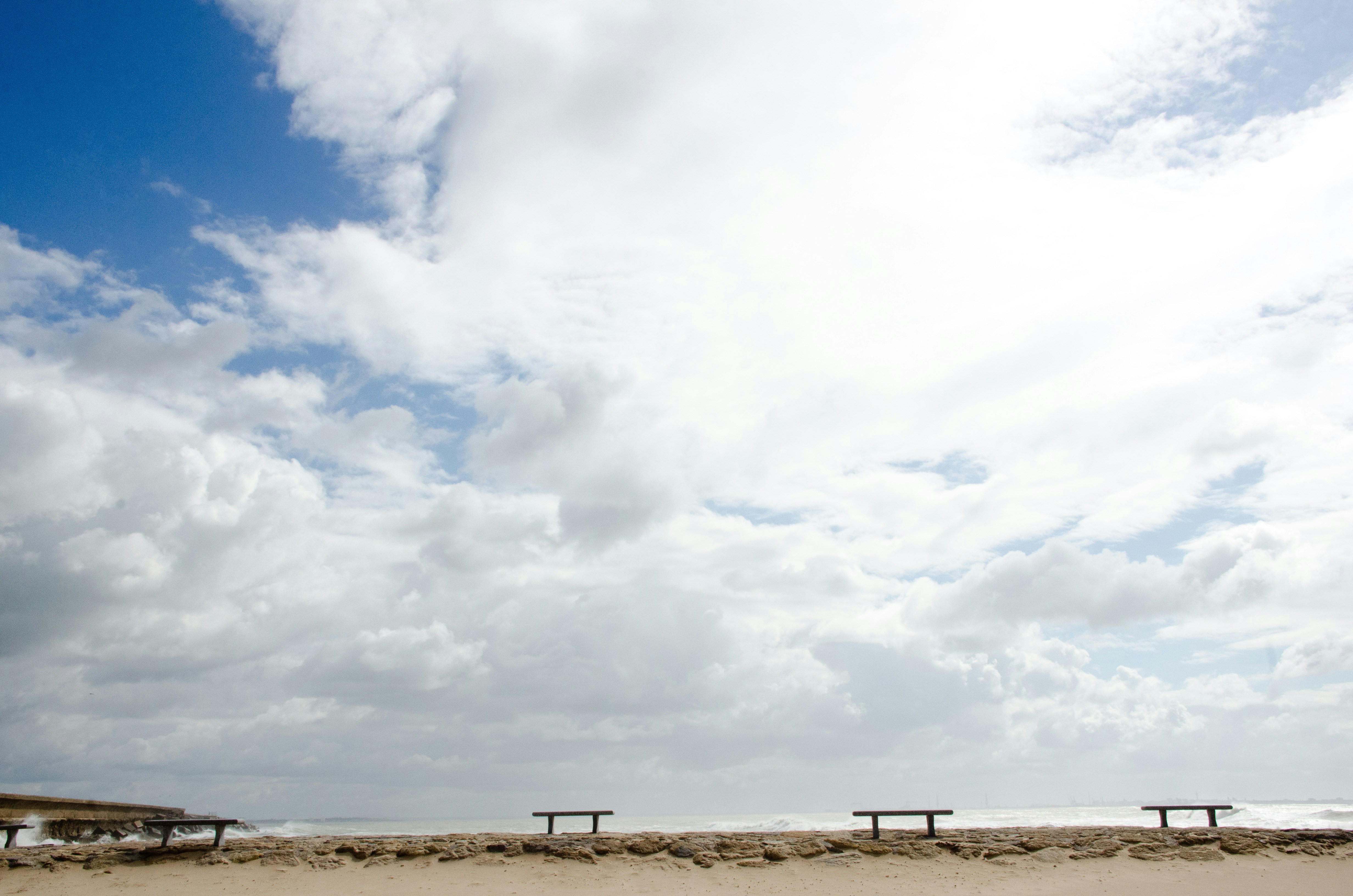 구름 아래 모래사장에 있는 빈 벤치 3개