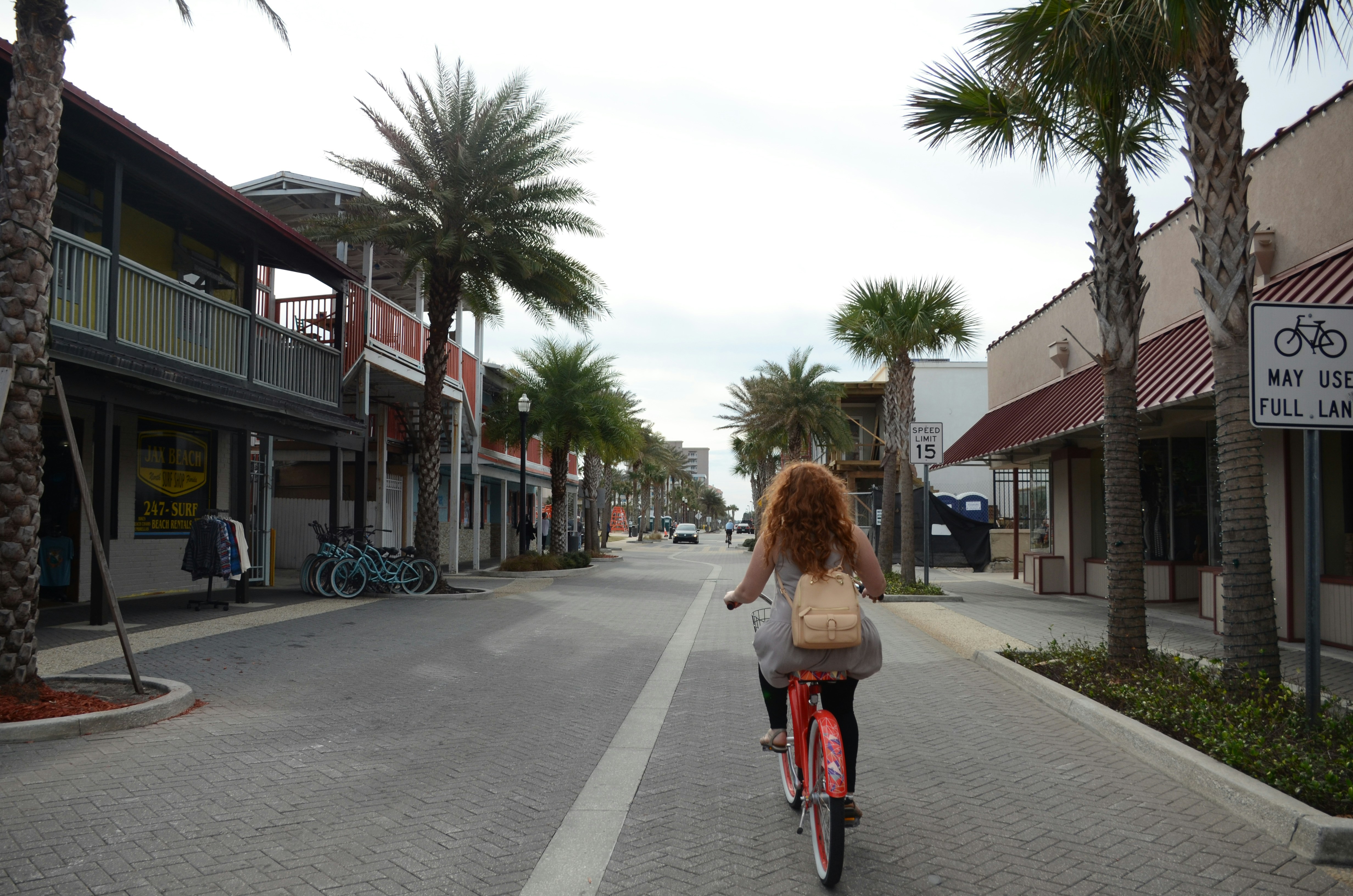 야자수가 있는 햇볕이 잘 드는 거리를 자전거를 타는 여성.