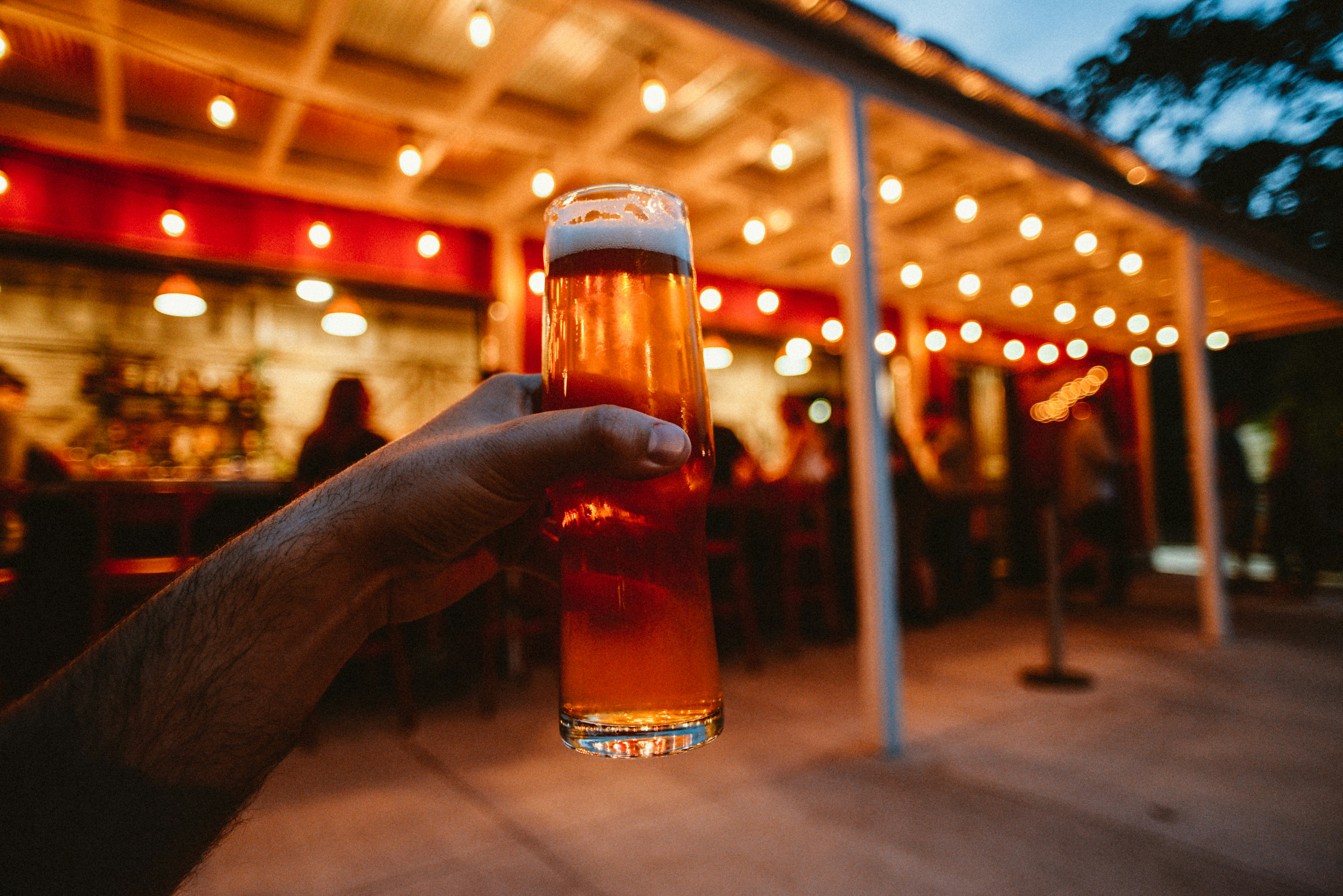 스트링 조명이 달린 맥주 한 잔을 손으로 들고 있는 모습