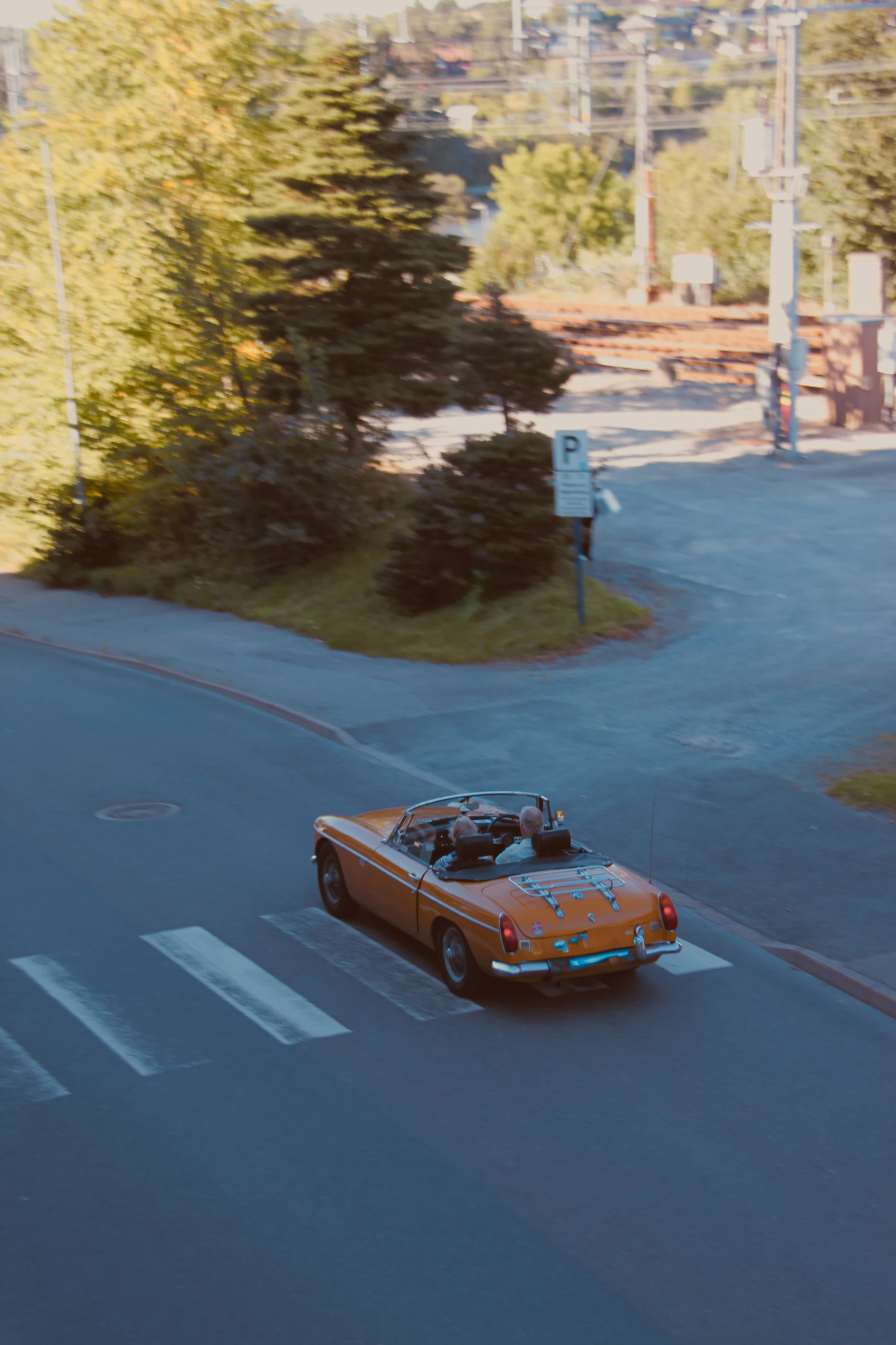 Orange convertible driving across a crosswalk.