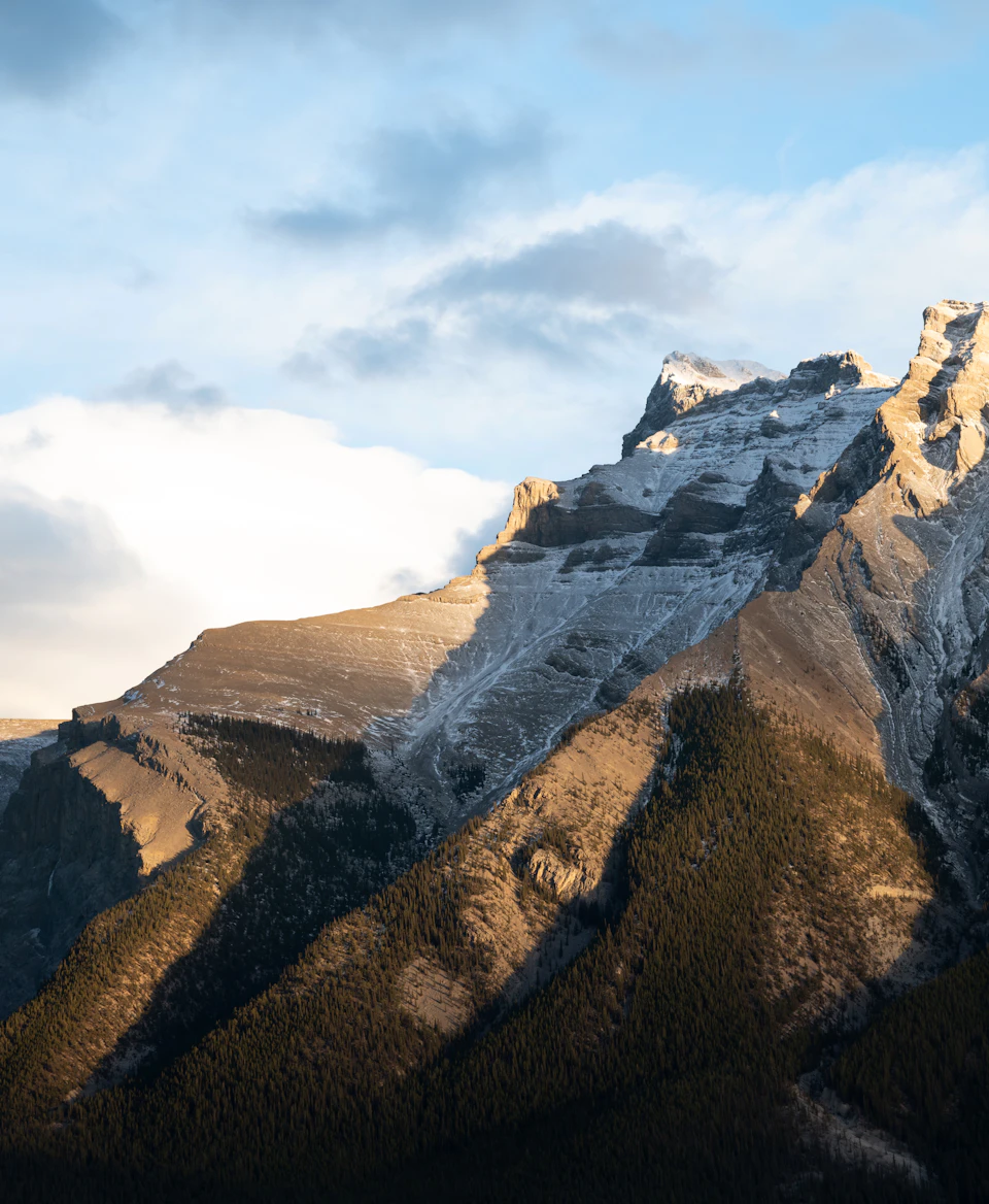Majestic mountain range with snow-capped peaks and lush green forest below in sunlight