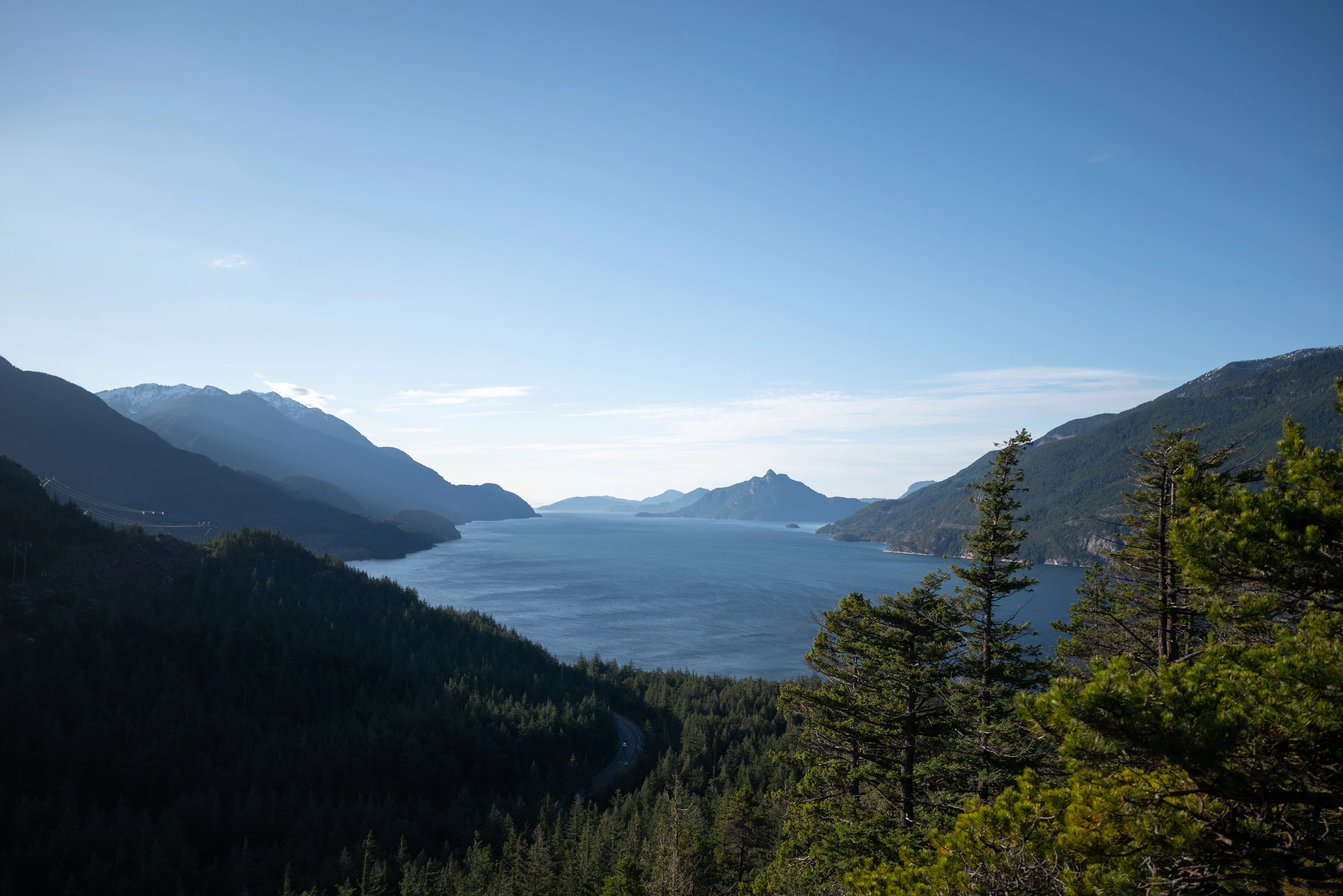 The Sea-to-Sky Highway threading along the forested shore of Howe Sound near Squamish, the fjord opening out between blue layered mountains