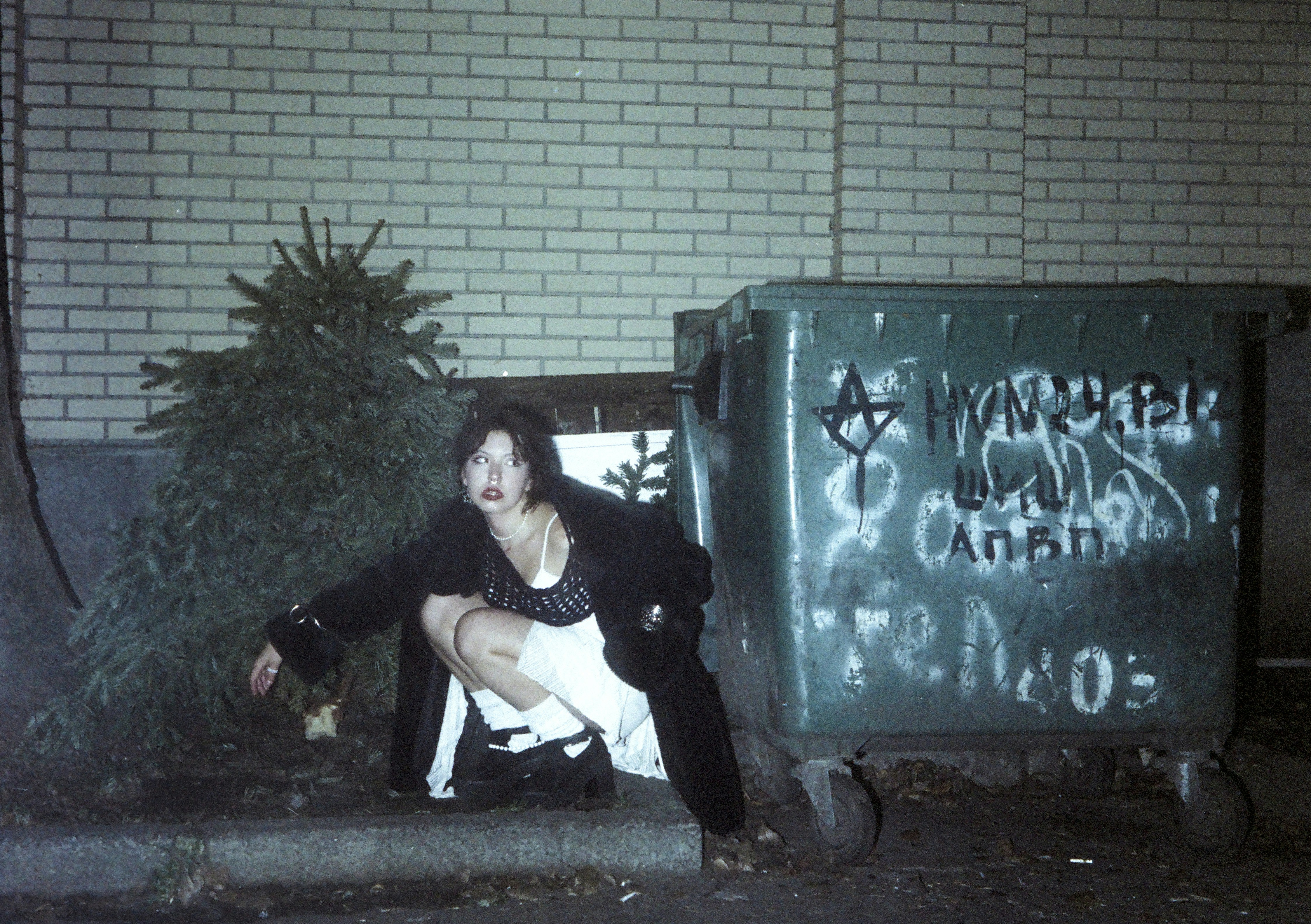 Frau hockt neben einem mit Graffiti beschmierten Müllcontainer.