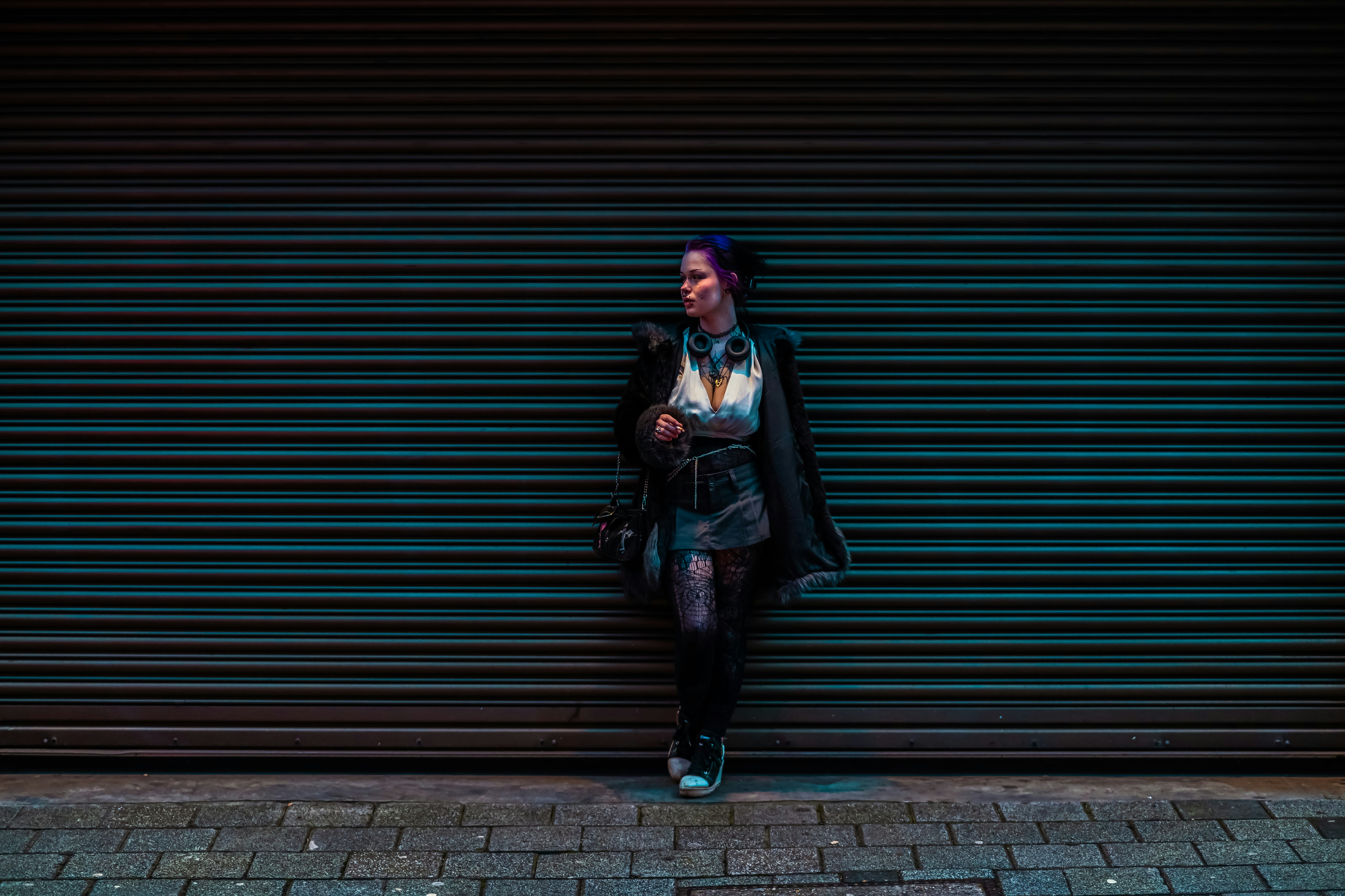 Woman with purple hair leaning against a dark blue wall.