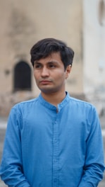 A man in a blue collared shirt stands outdoors.