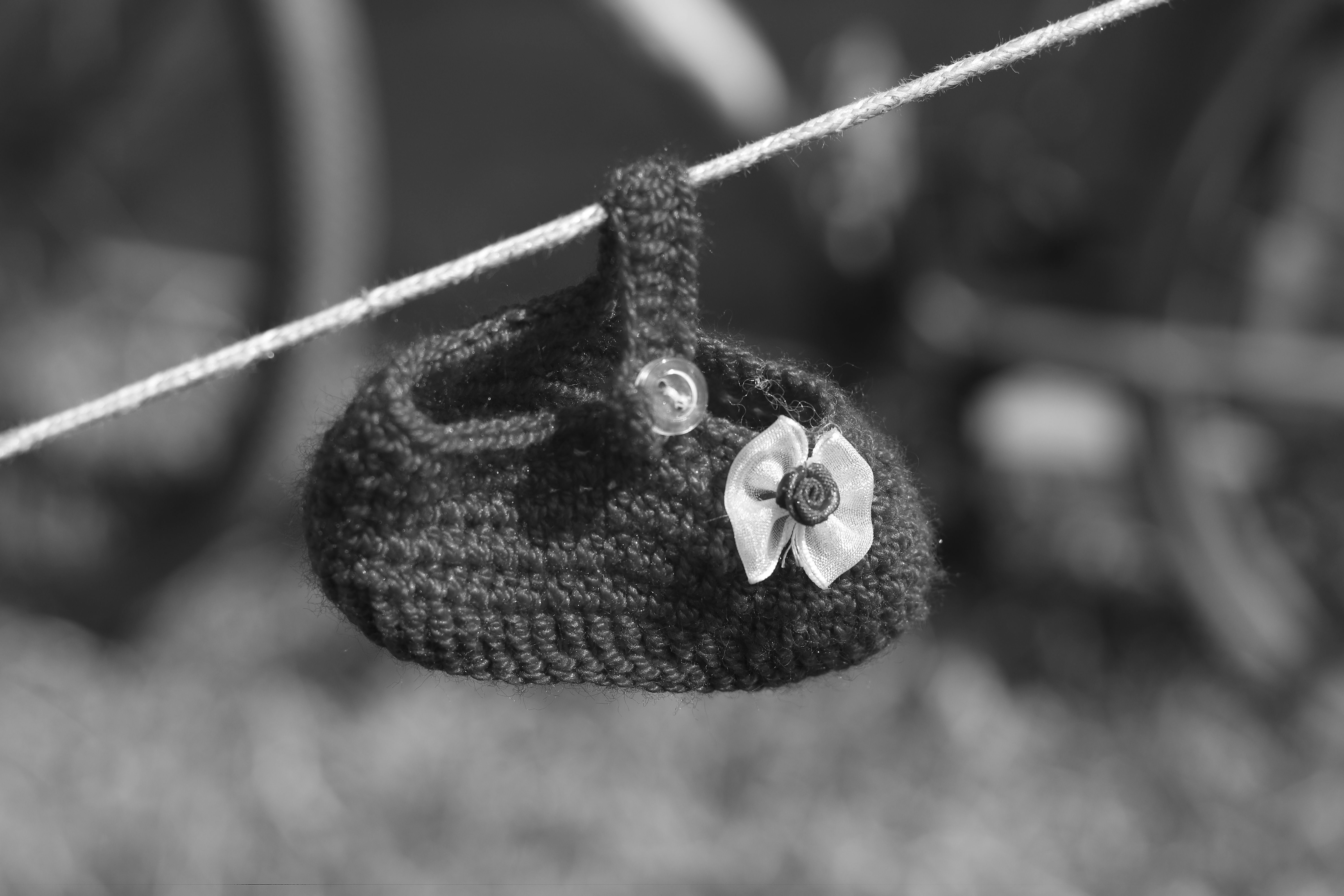Crocheted baby shoe with flower detail hangs on line.