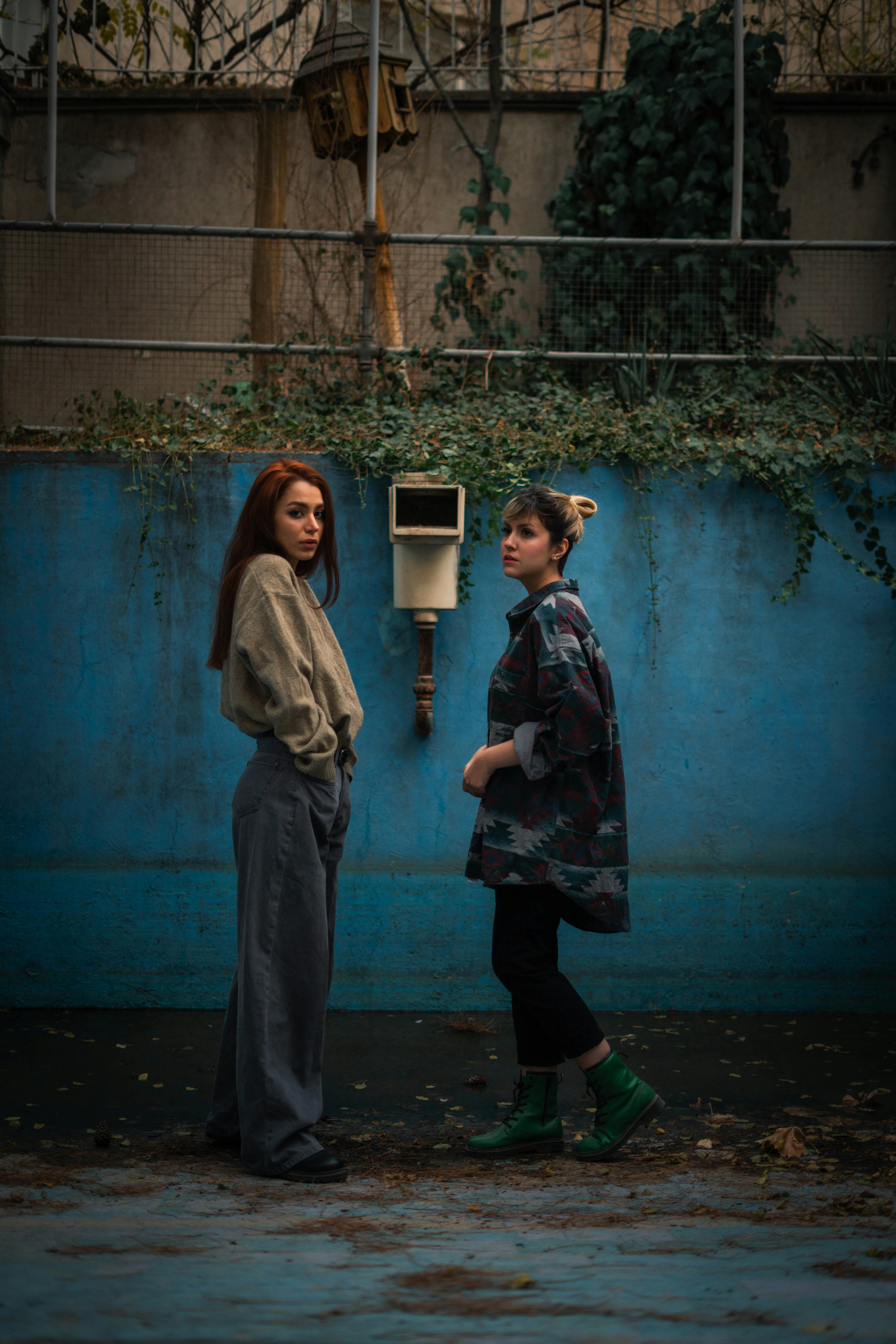 Two young women standing against a blue wall