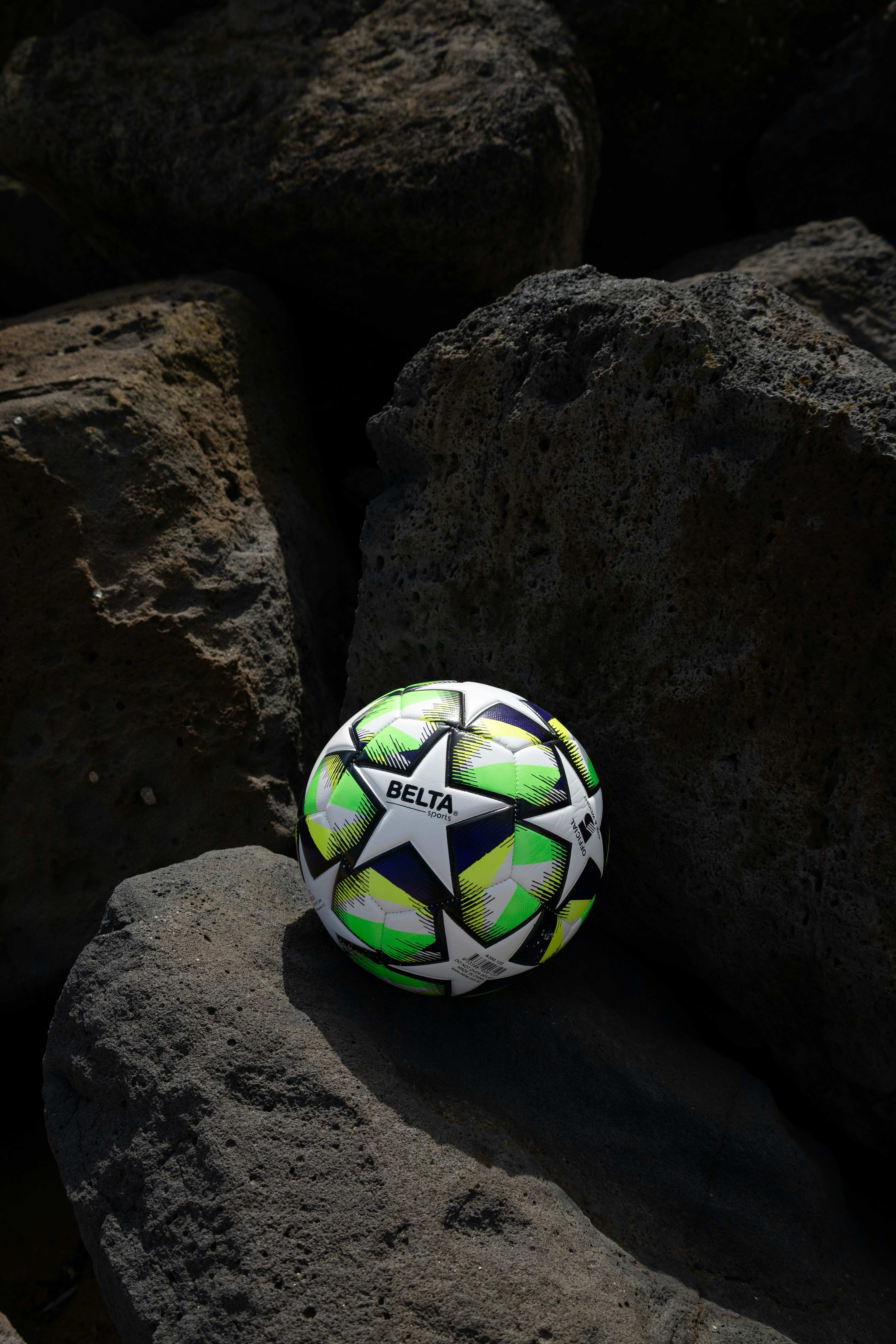 Soccer ball resting on dark, textured rocks.