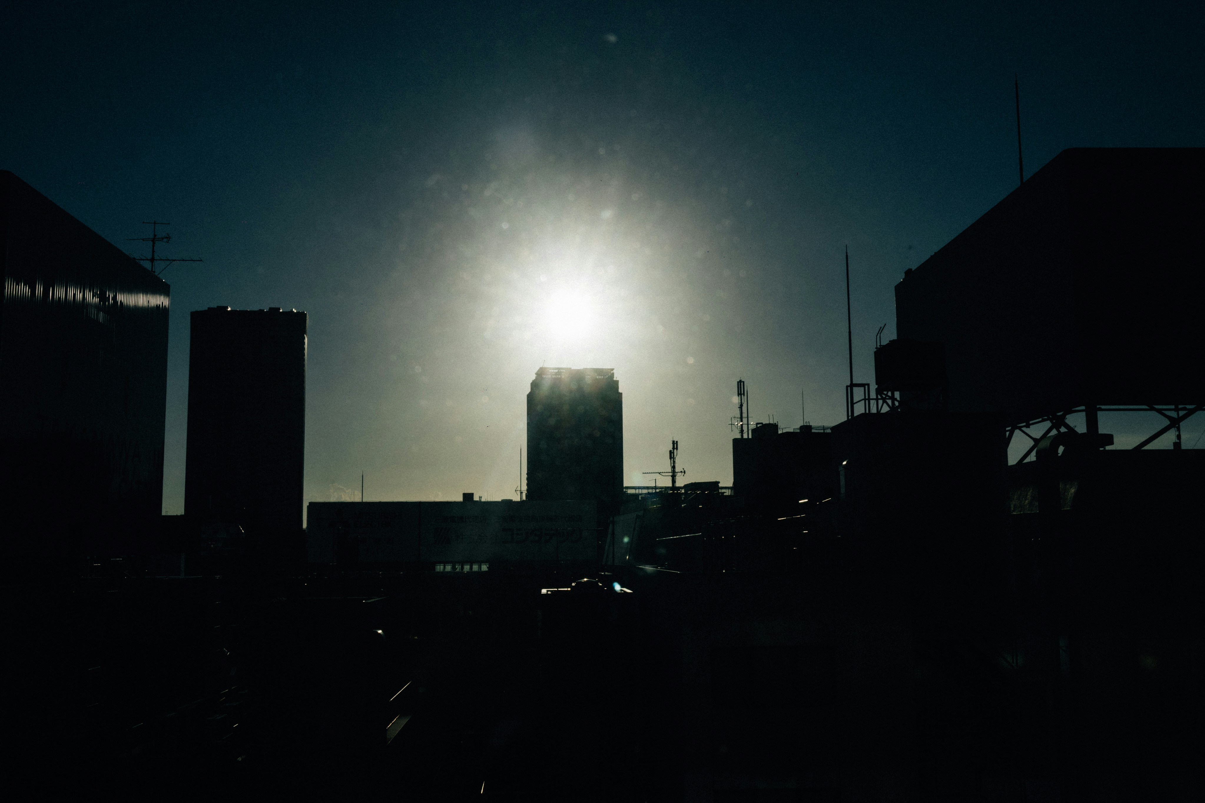 Bright sun behind silhouetted buildings at dusk.