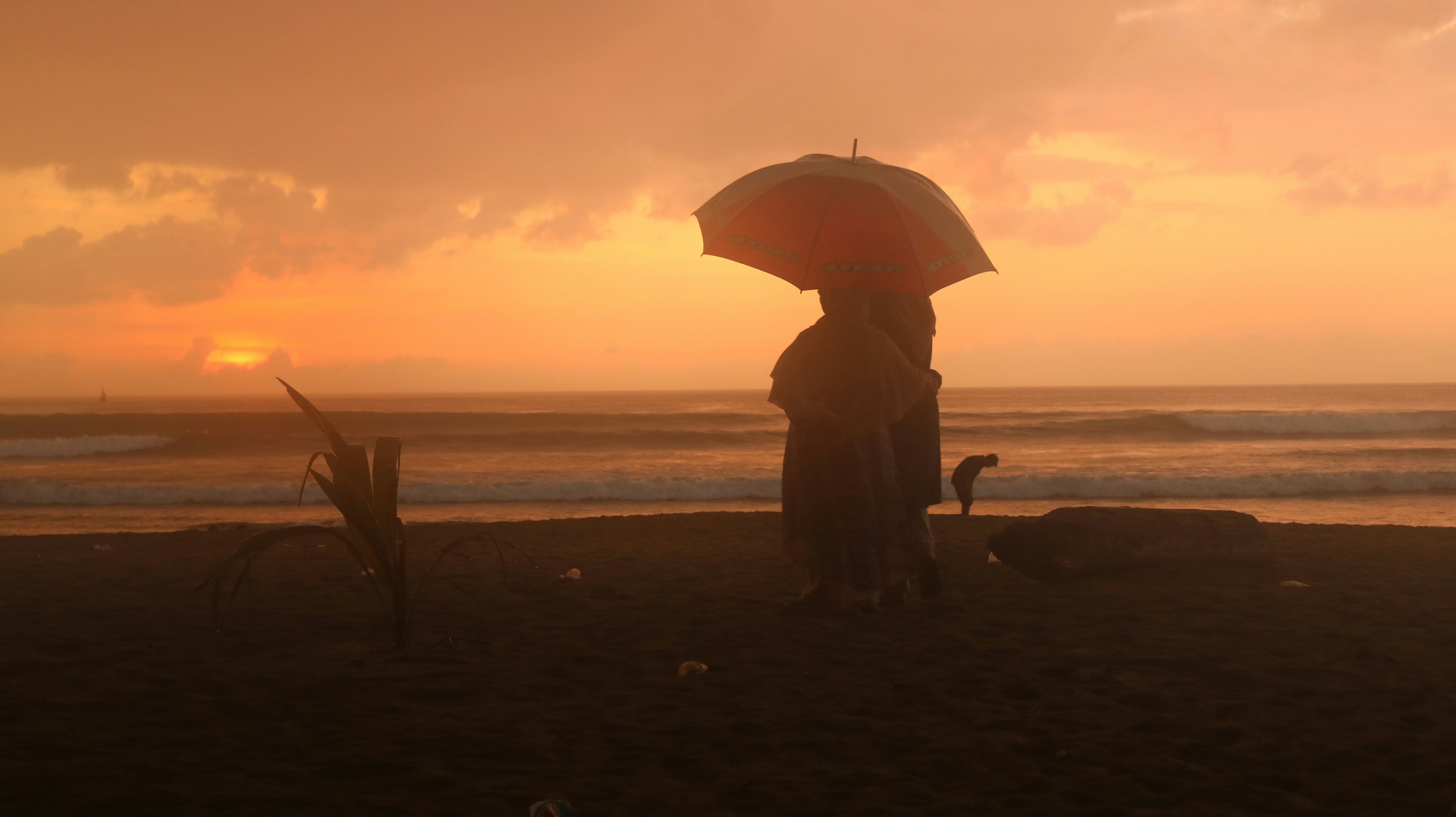 Silhouette of people with umbrella on beach at sunset