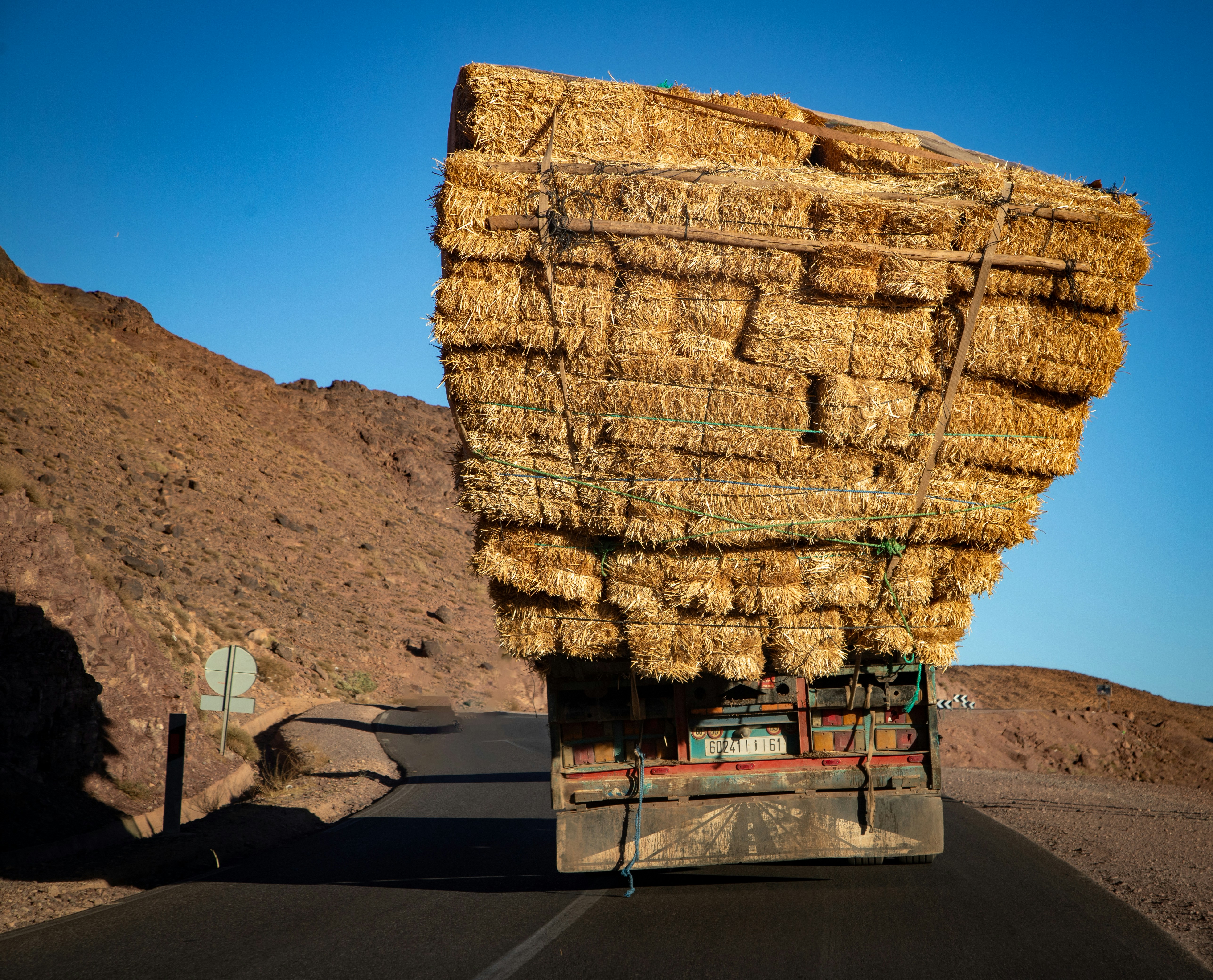 Camion sovraccarico di balle di fieno su una strada deserta.
