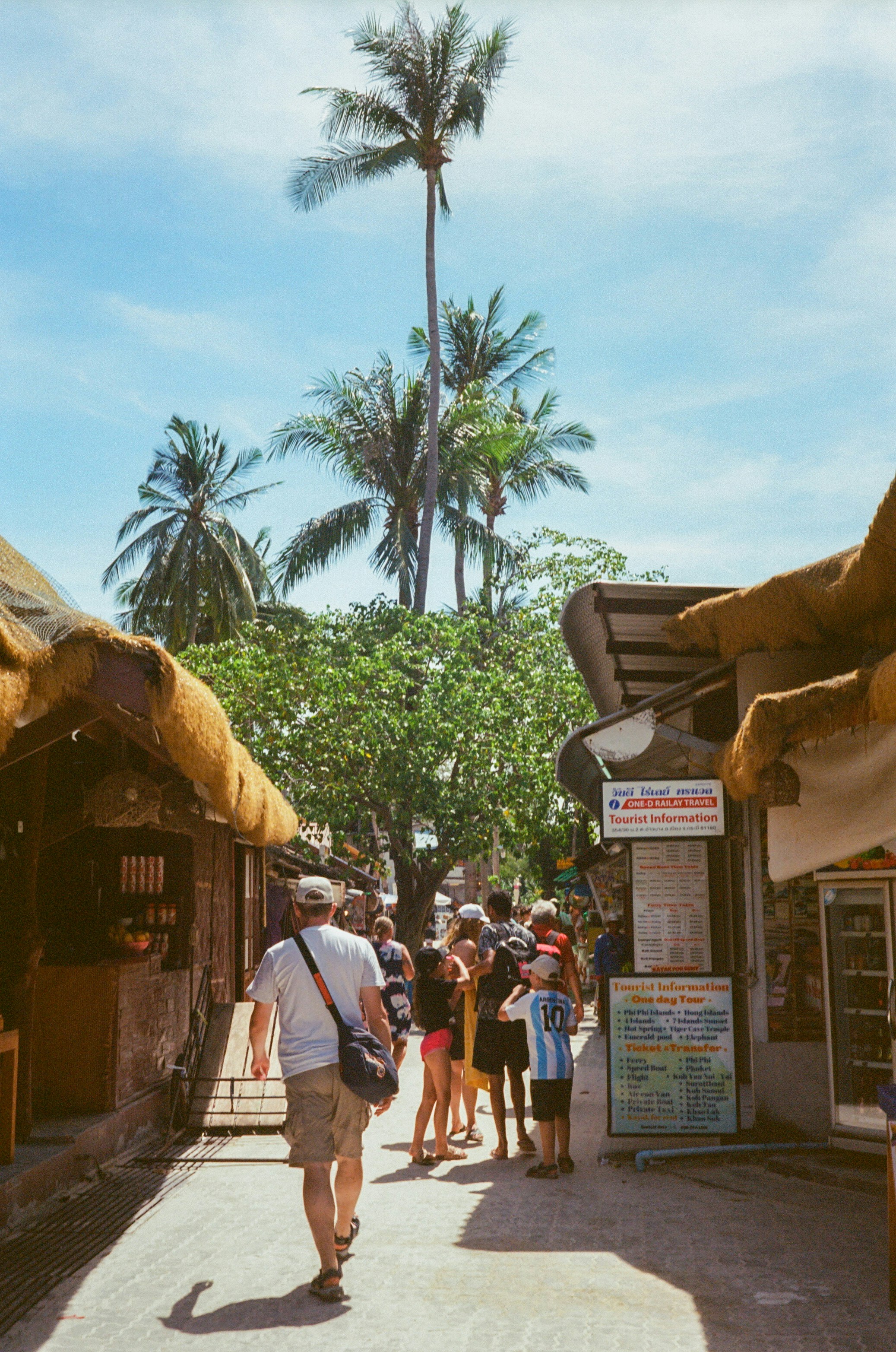 People walking down a tropical street lined with shops.