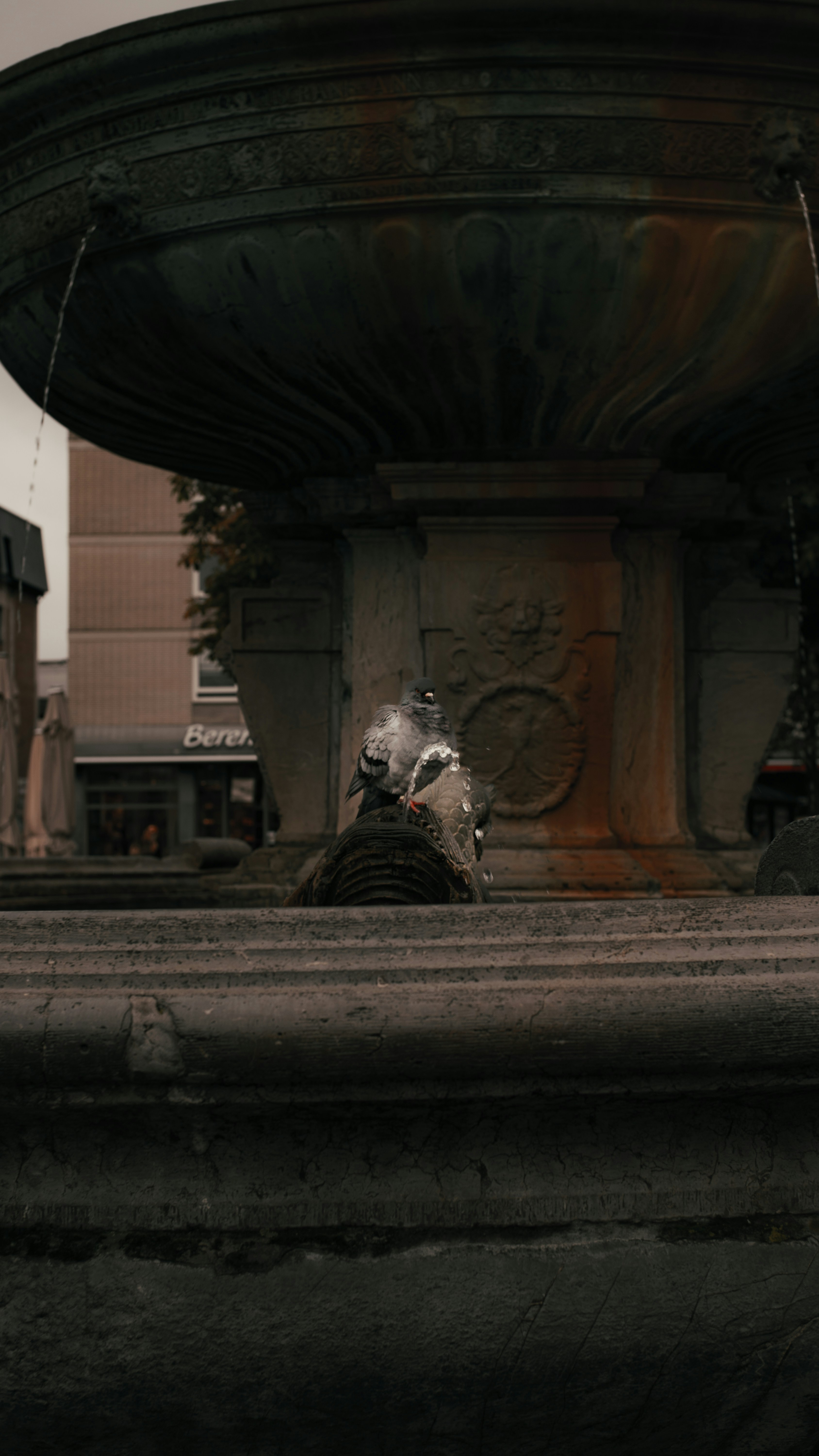 Water flows from an ornate stone fountain in a city.