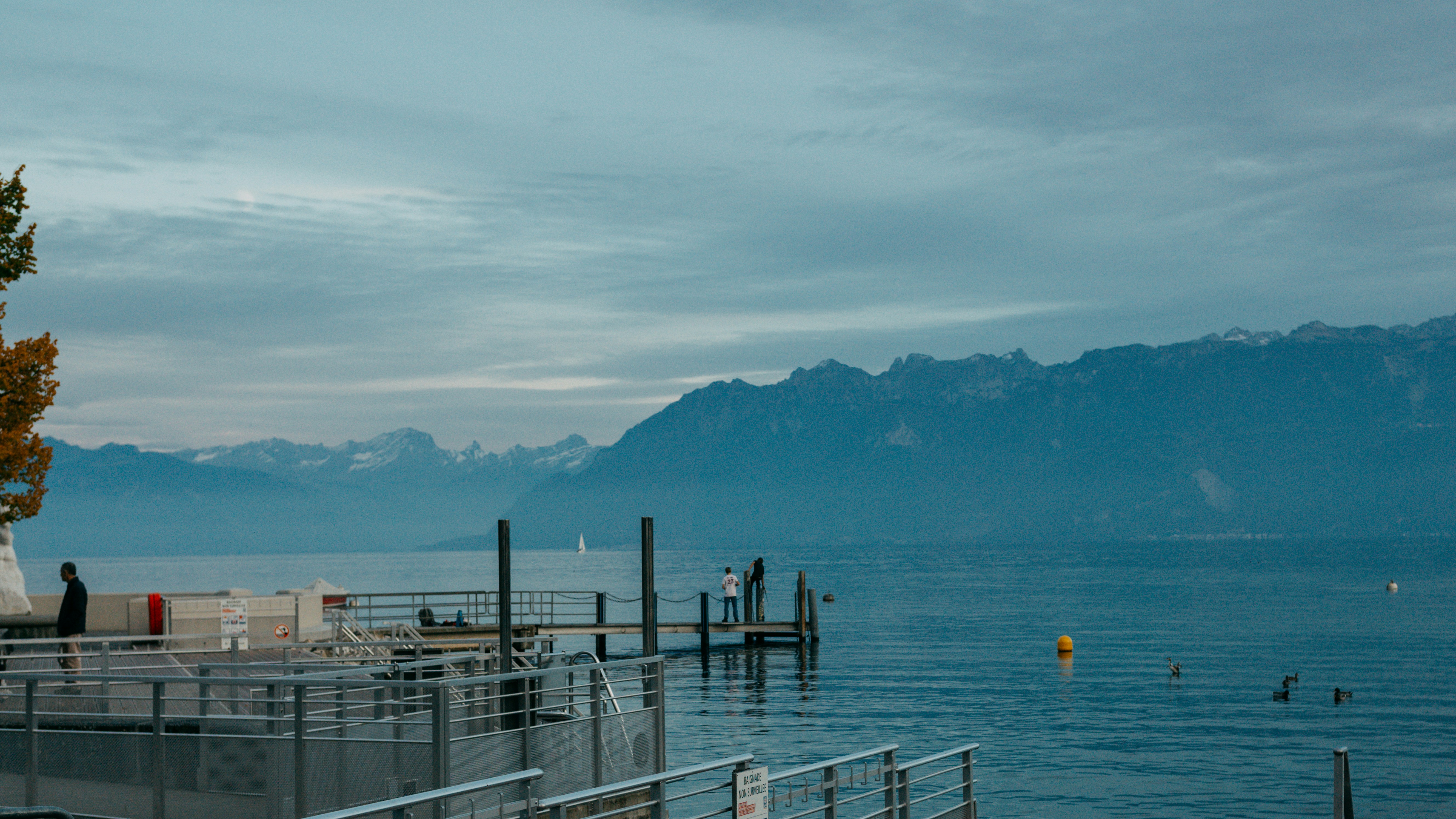 Calm lake with distant mountains under cloudy sky.