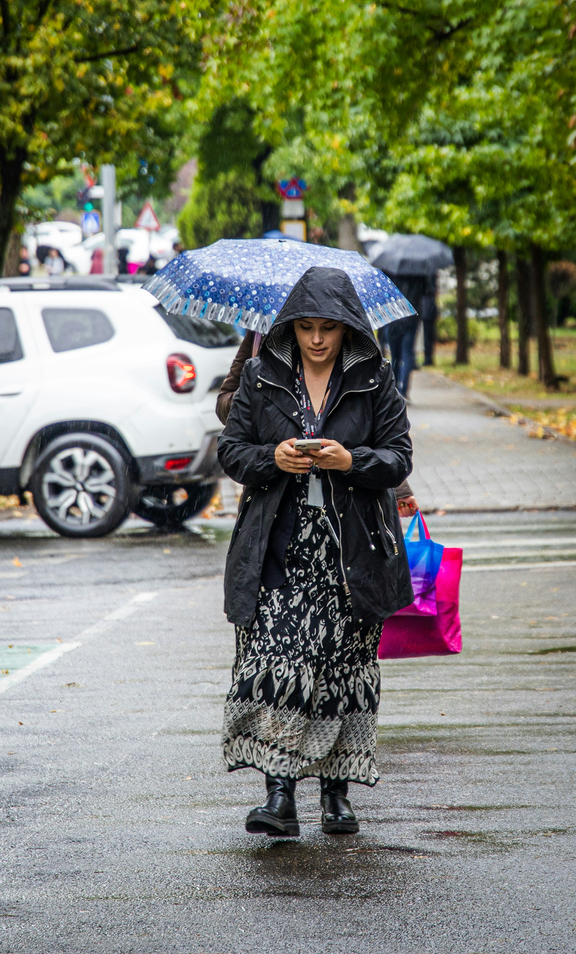 Donna con ombrello che guarda il telefono sotto la pioggia