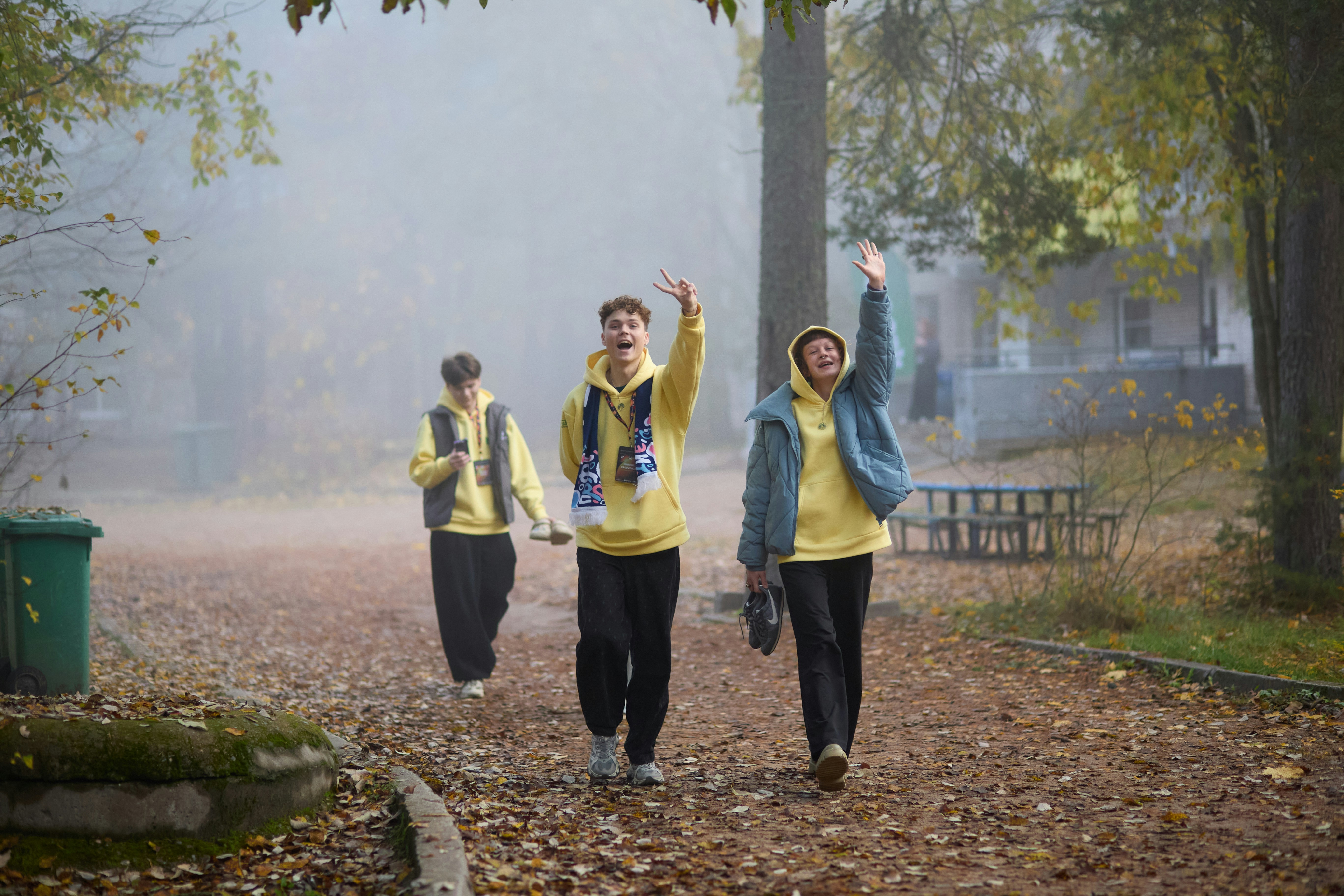 Three people walking in a park with yellow jackets.