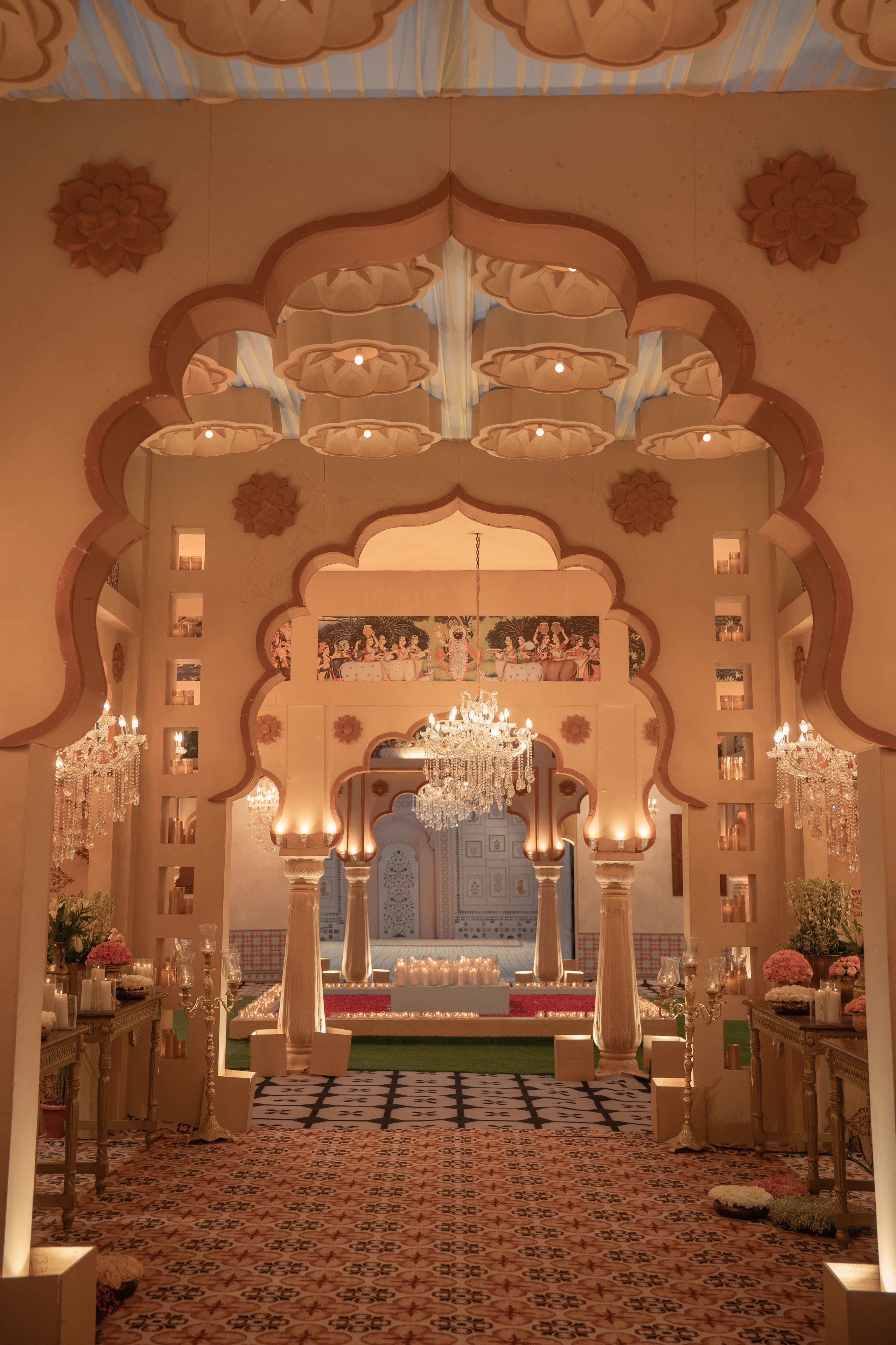 Ornate carved archway mandap lit by chandeliers with guest seating