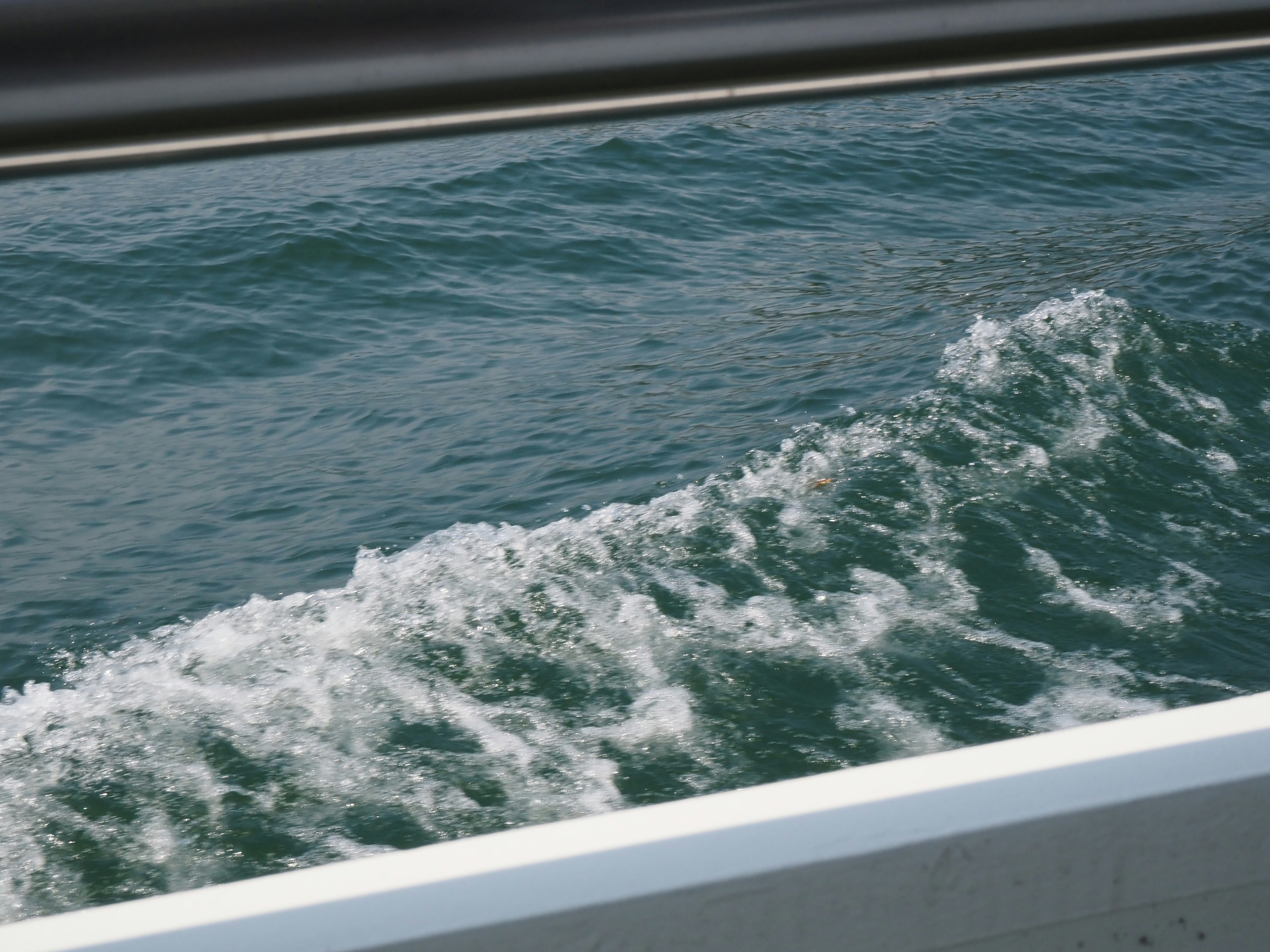 Weiße Kielwasser von Boot, das sich durch blaues Wasser bewegt