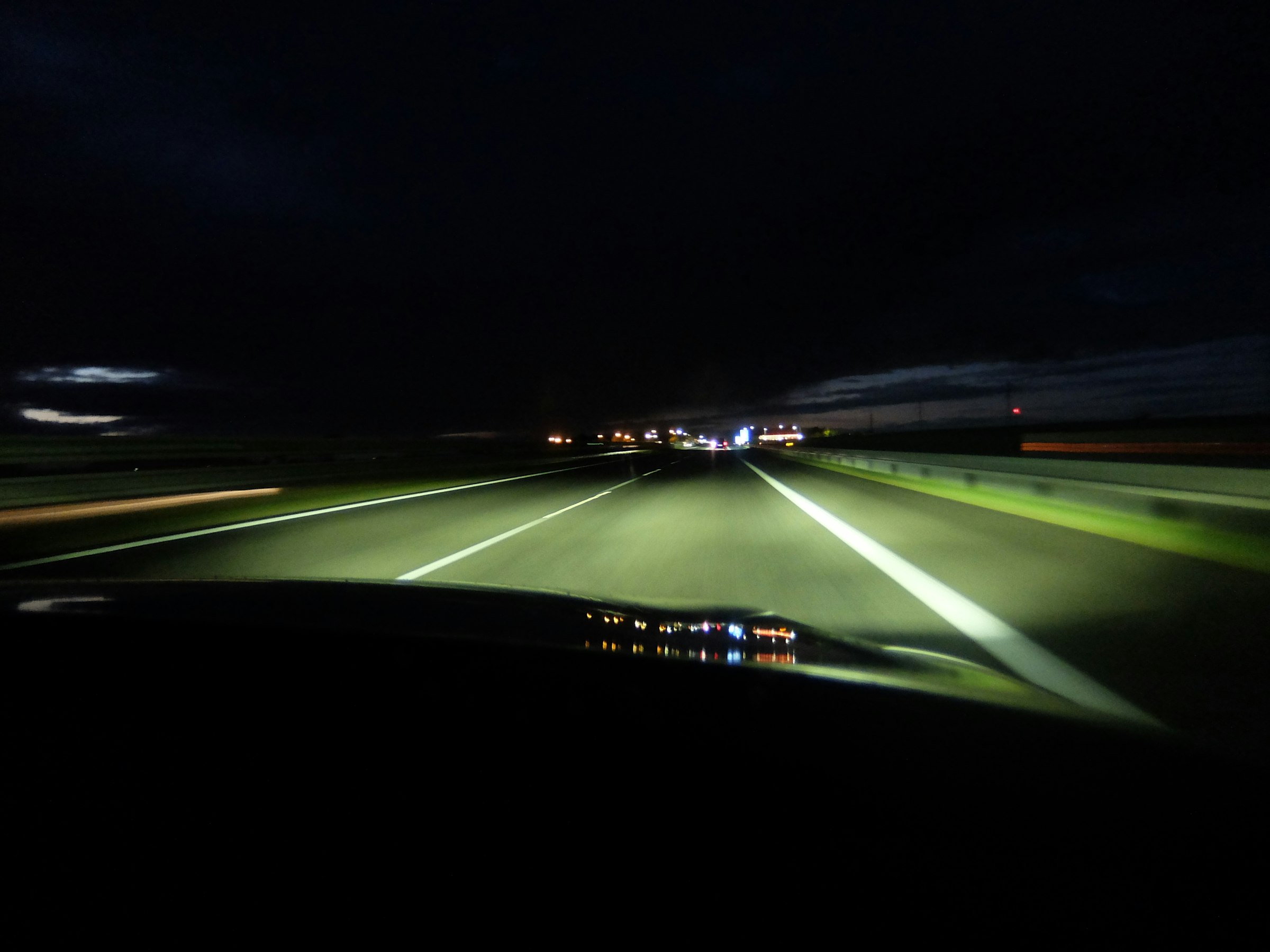 Carretera de noche iluminada por los faros de un coche.