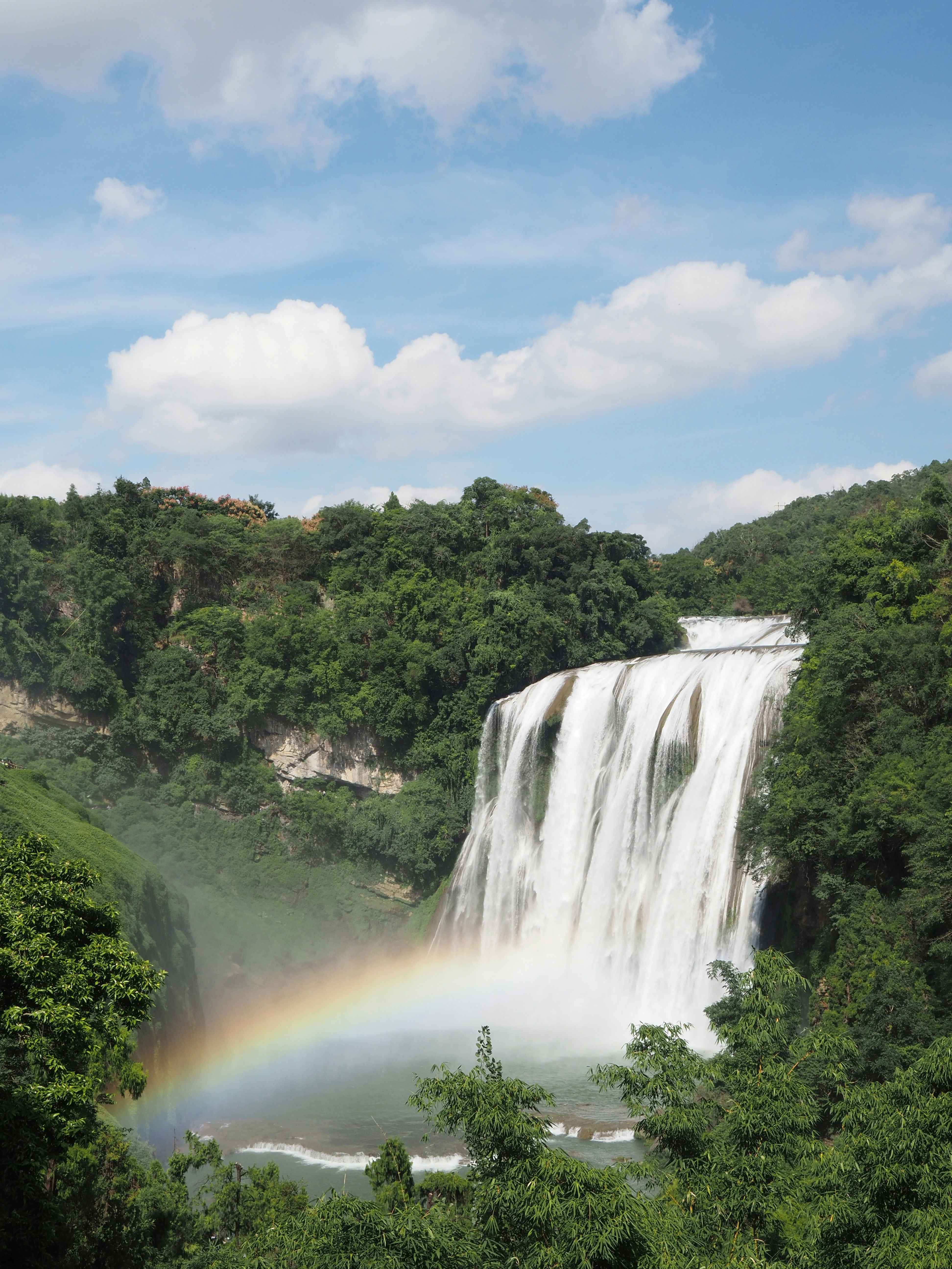 Une cascade majestueuse tombe en cascade sur les falaises avec un arc-en-ciel.