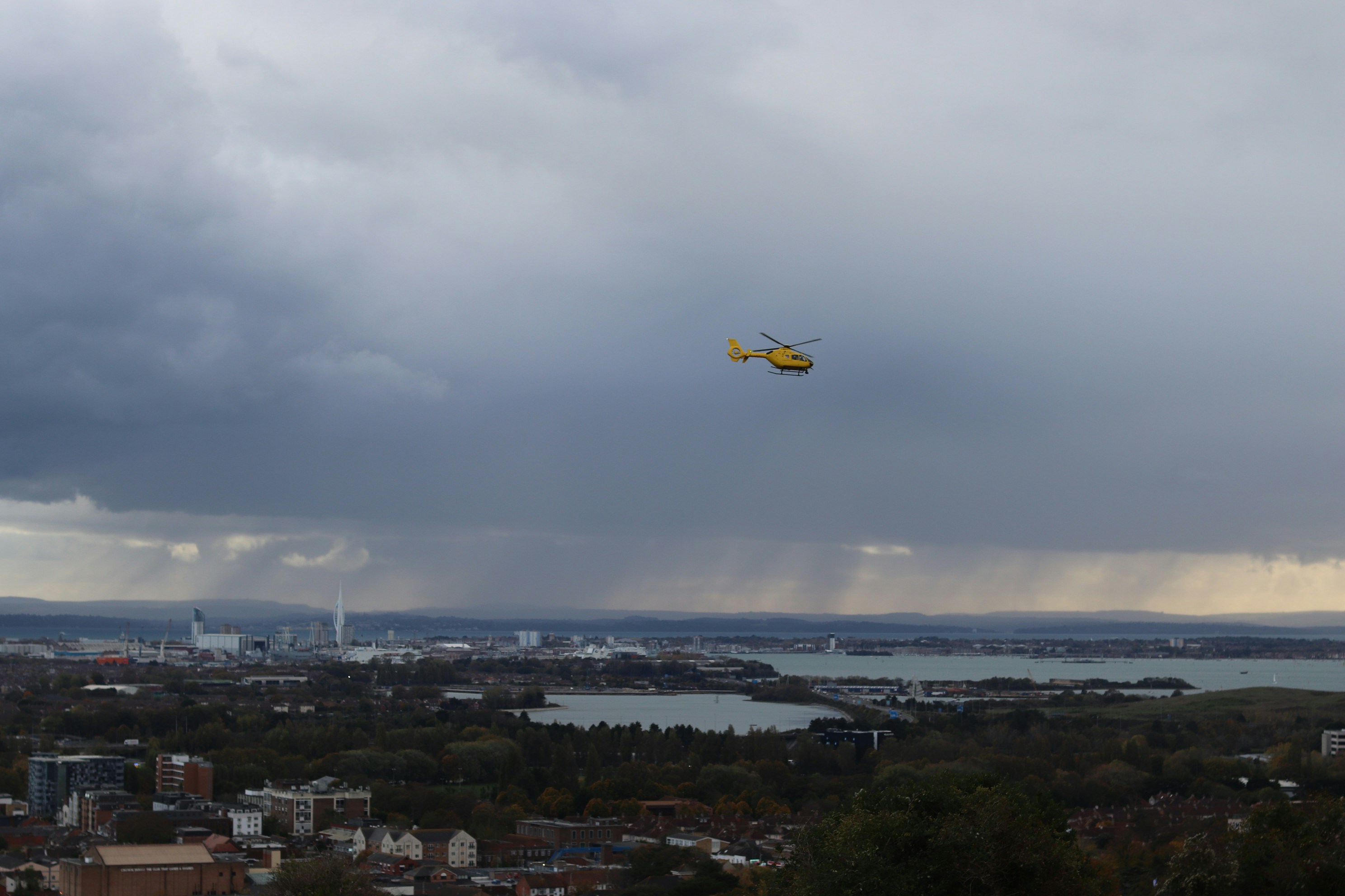 Yellow helicopter flies over city under stormy sky