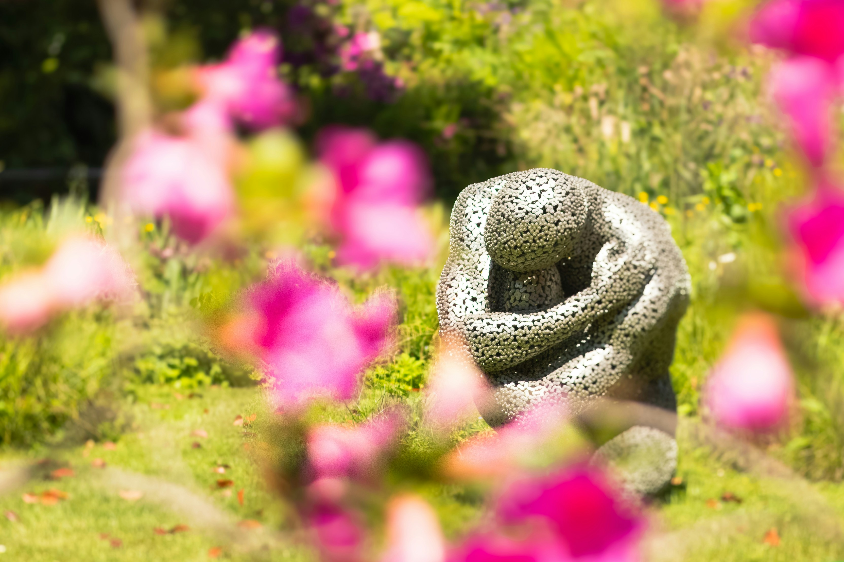 Sculpture in a garden surrounded by pink flowers.