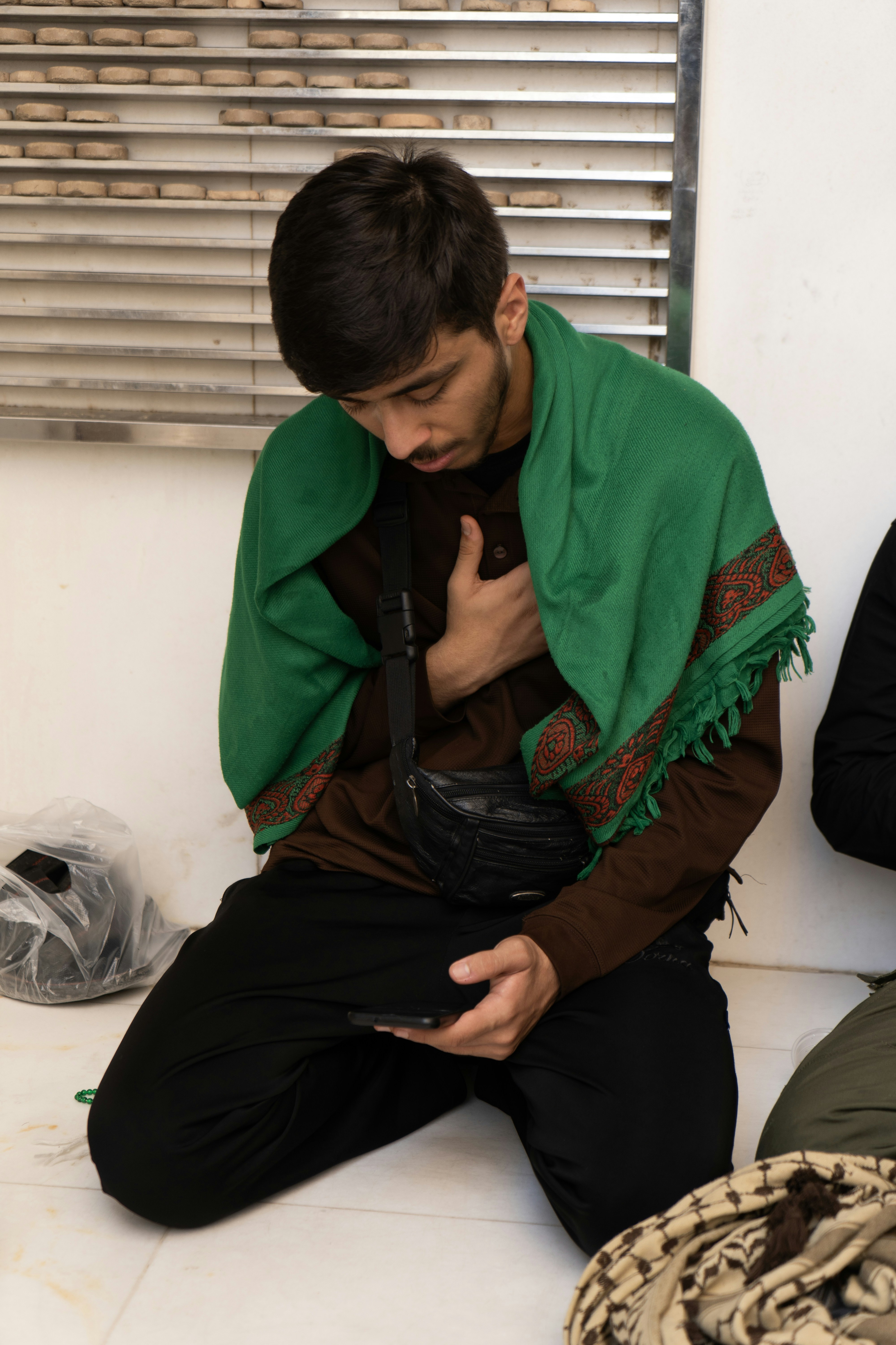 Man in green scarf praying while looking at phone