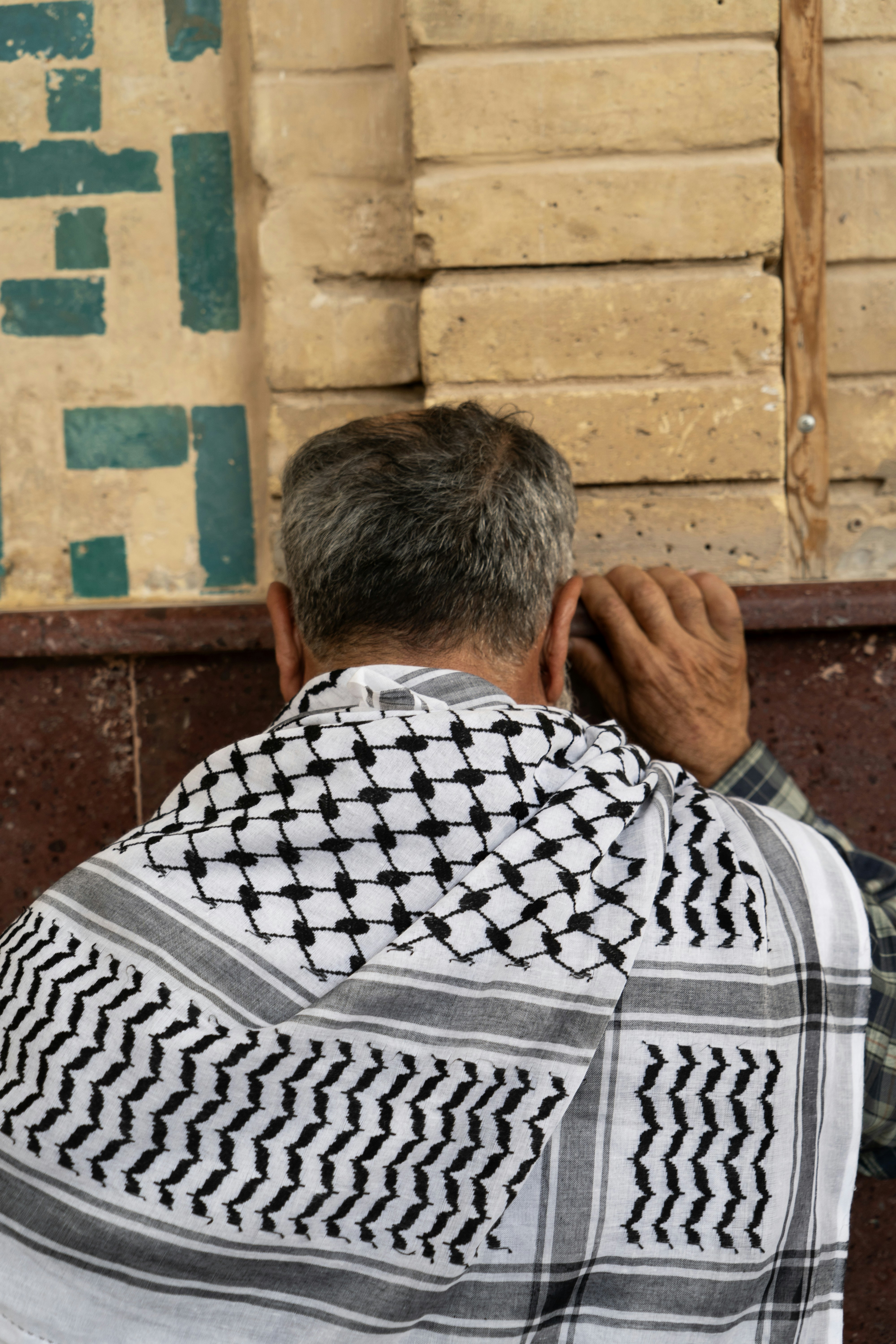 Hombre vistiendo keffiyeh rezando contra la pared texturizada.
