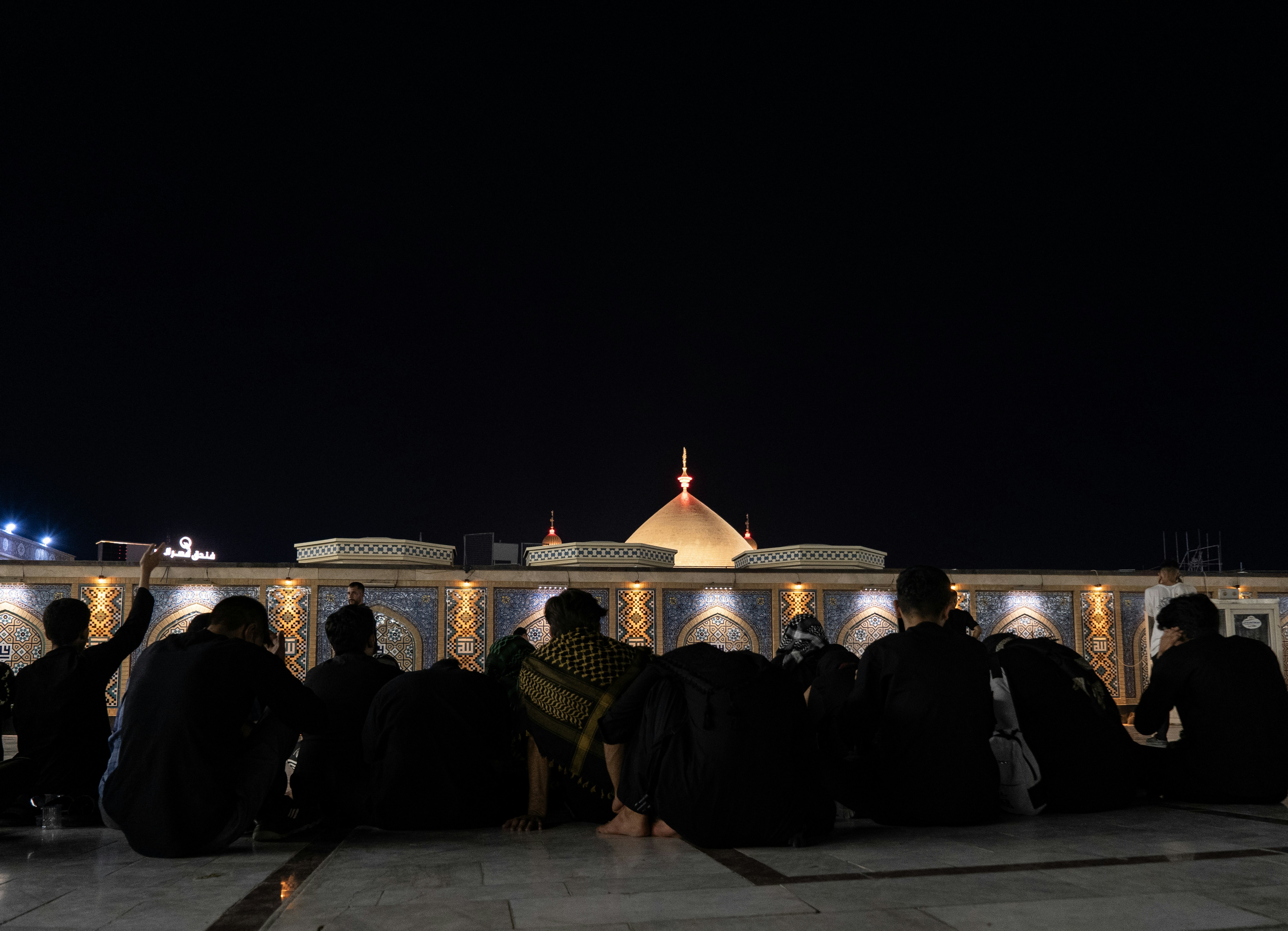 La nuit, des gens s’assoient devant un bâtiment en forme de dôme.
