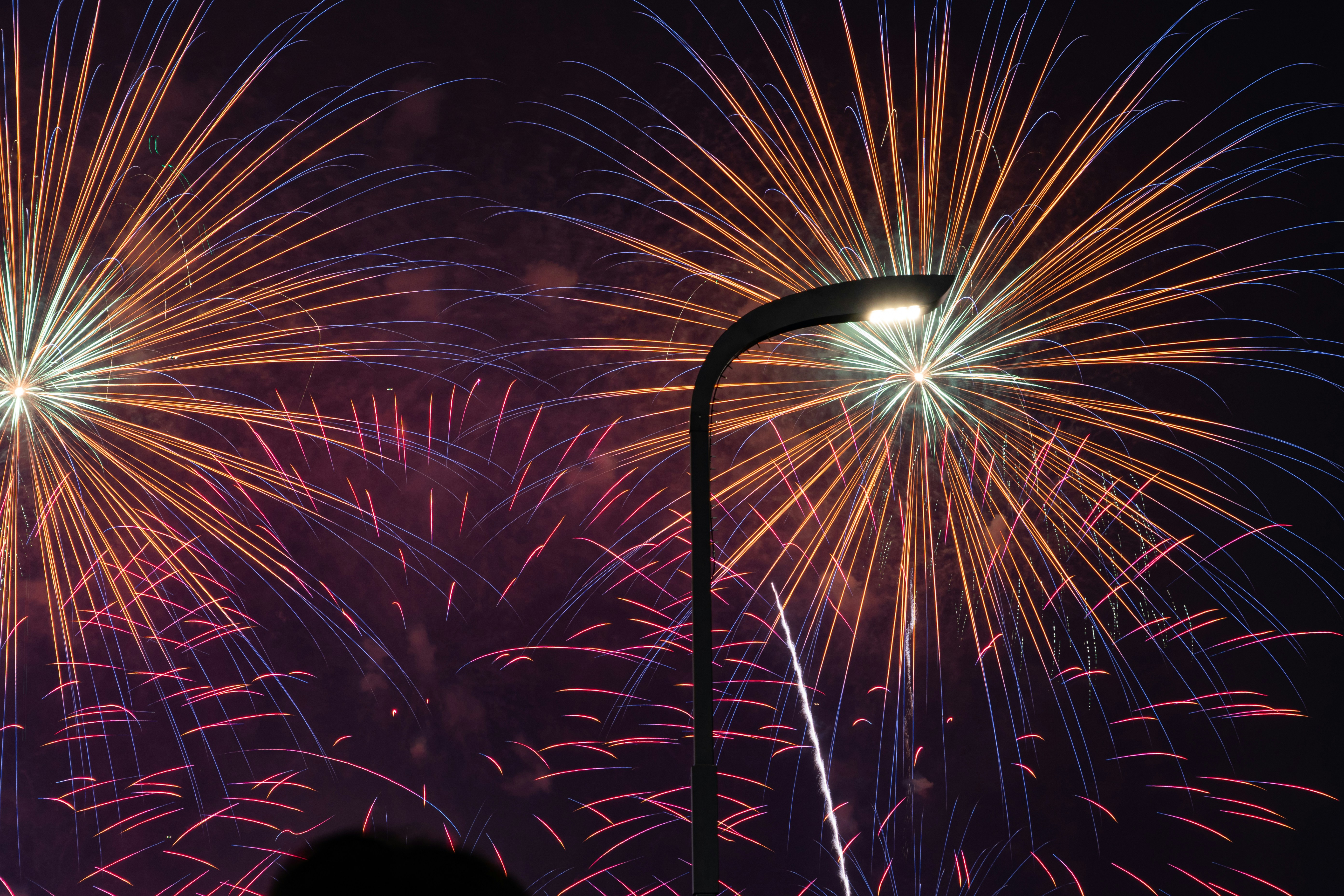 Bright fireworks explode behind a street lamp.