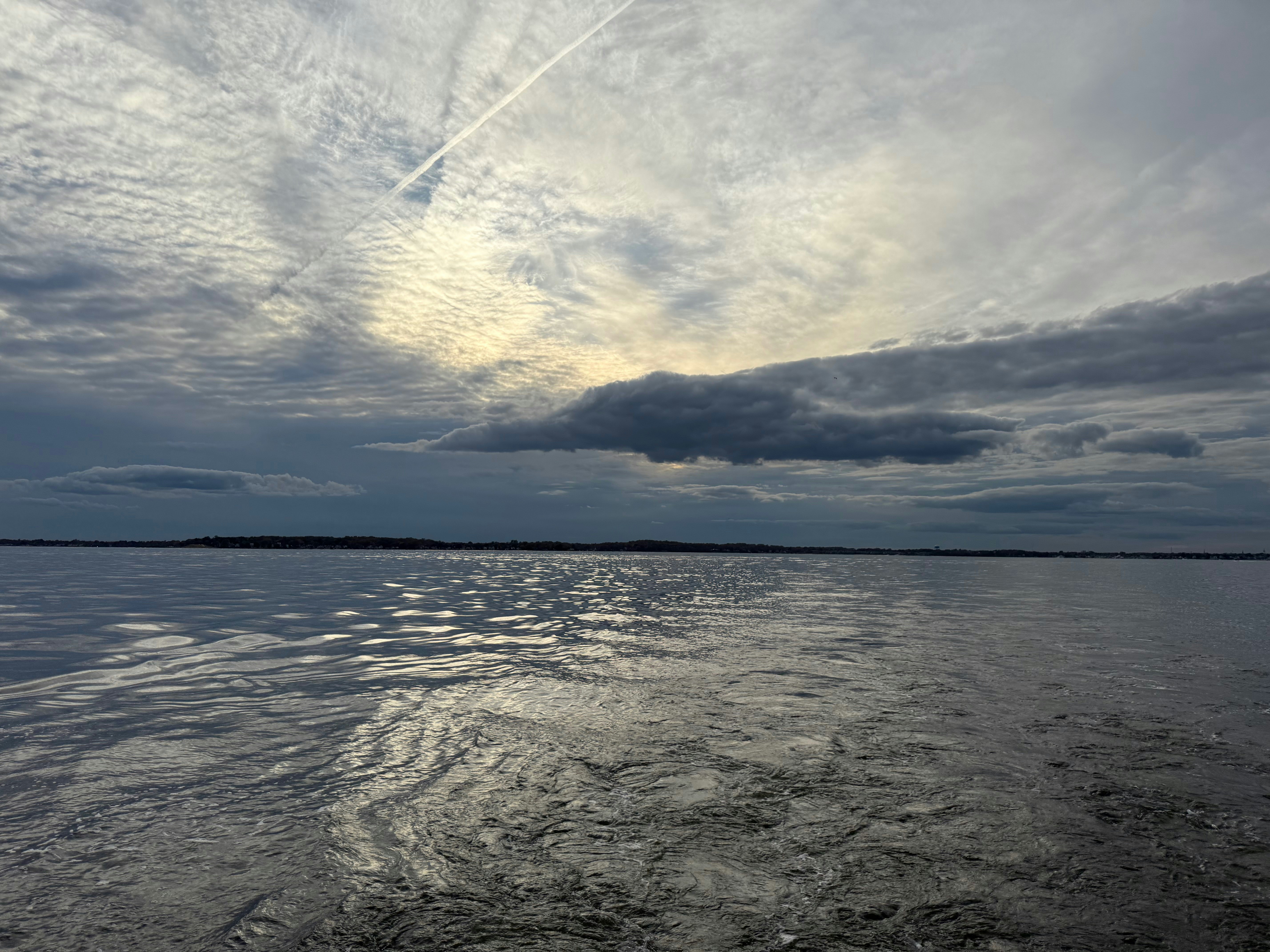 Calm water reflects a cloudy sky with a contrail.