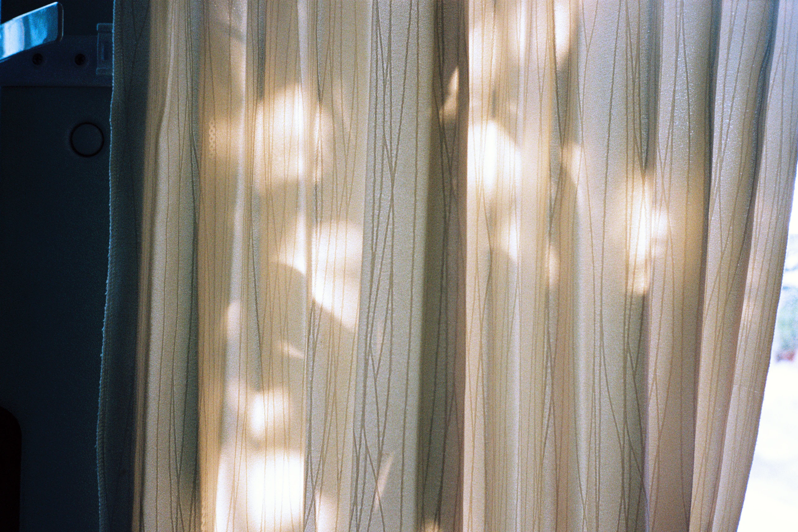 Midday sun breaking through sheer linen curtains in soft, moving patches.