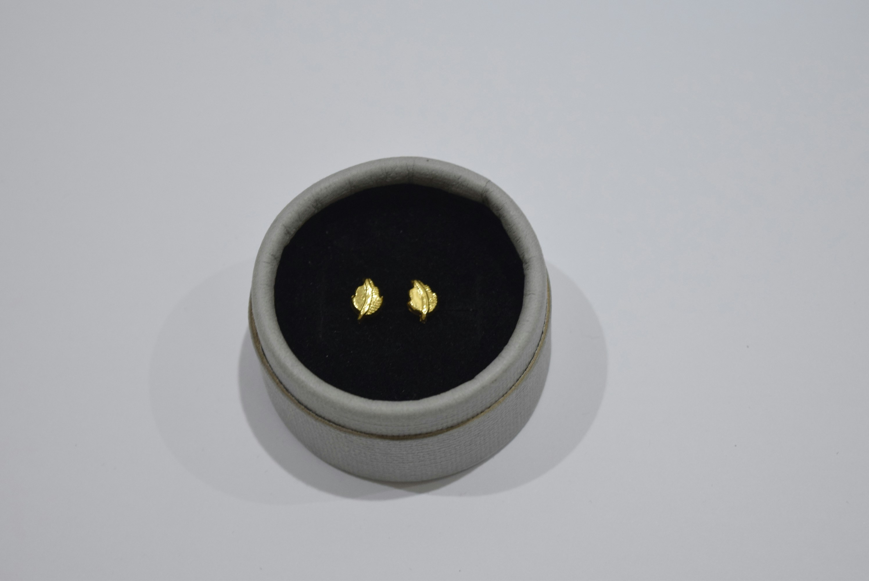 Small gold stud earrings in a round box
