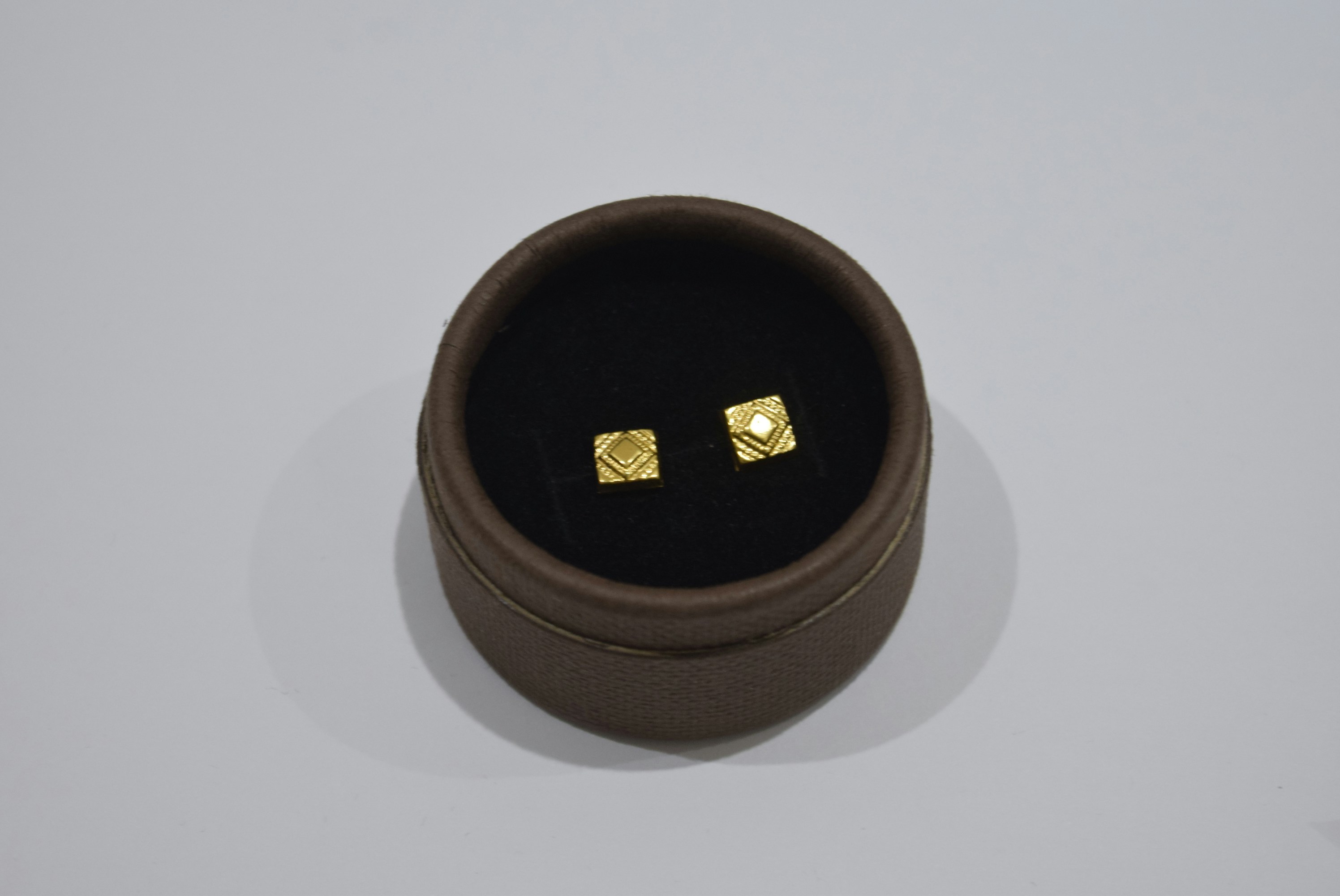 Two small gold square earrings in a box