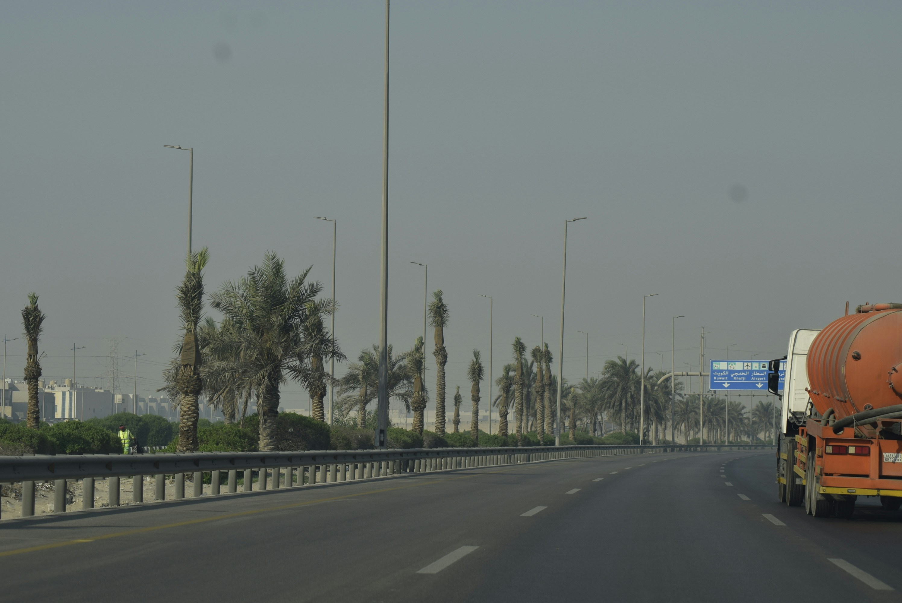 A highway with palm trees and a tanker truck.