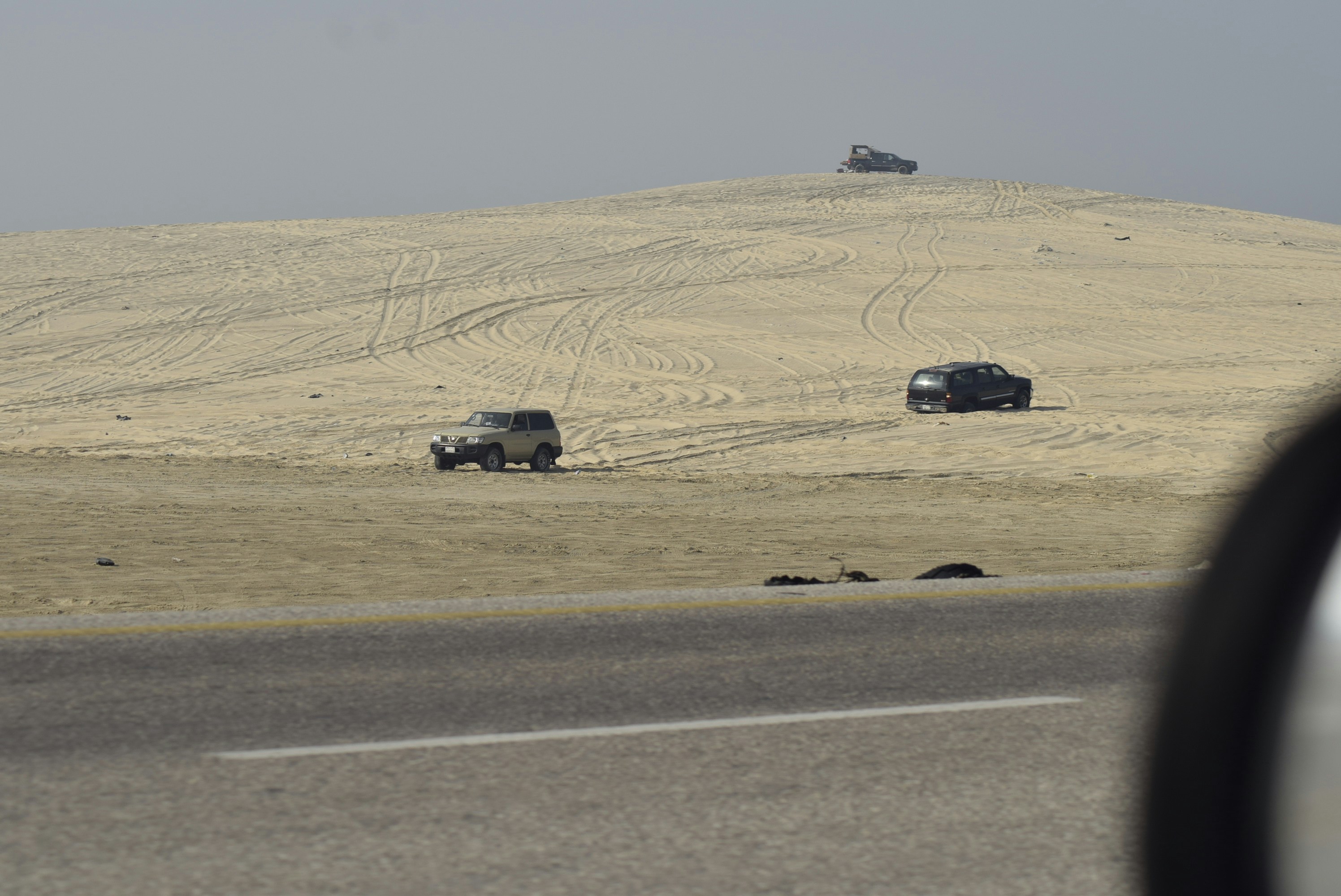 Several vehicles driving on a sandy, hilly terrain.
