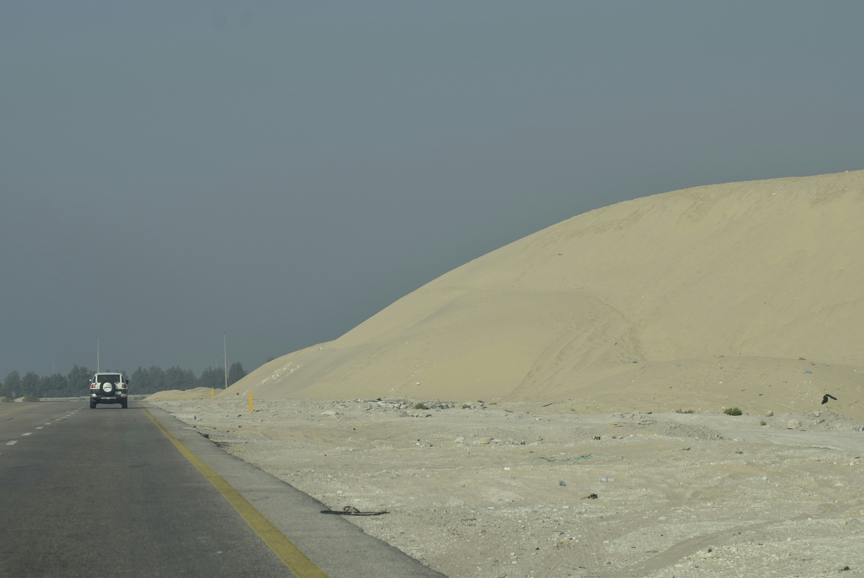 Une voiture roule sur une route à côté de dunes de sable.