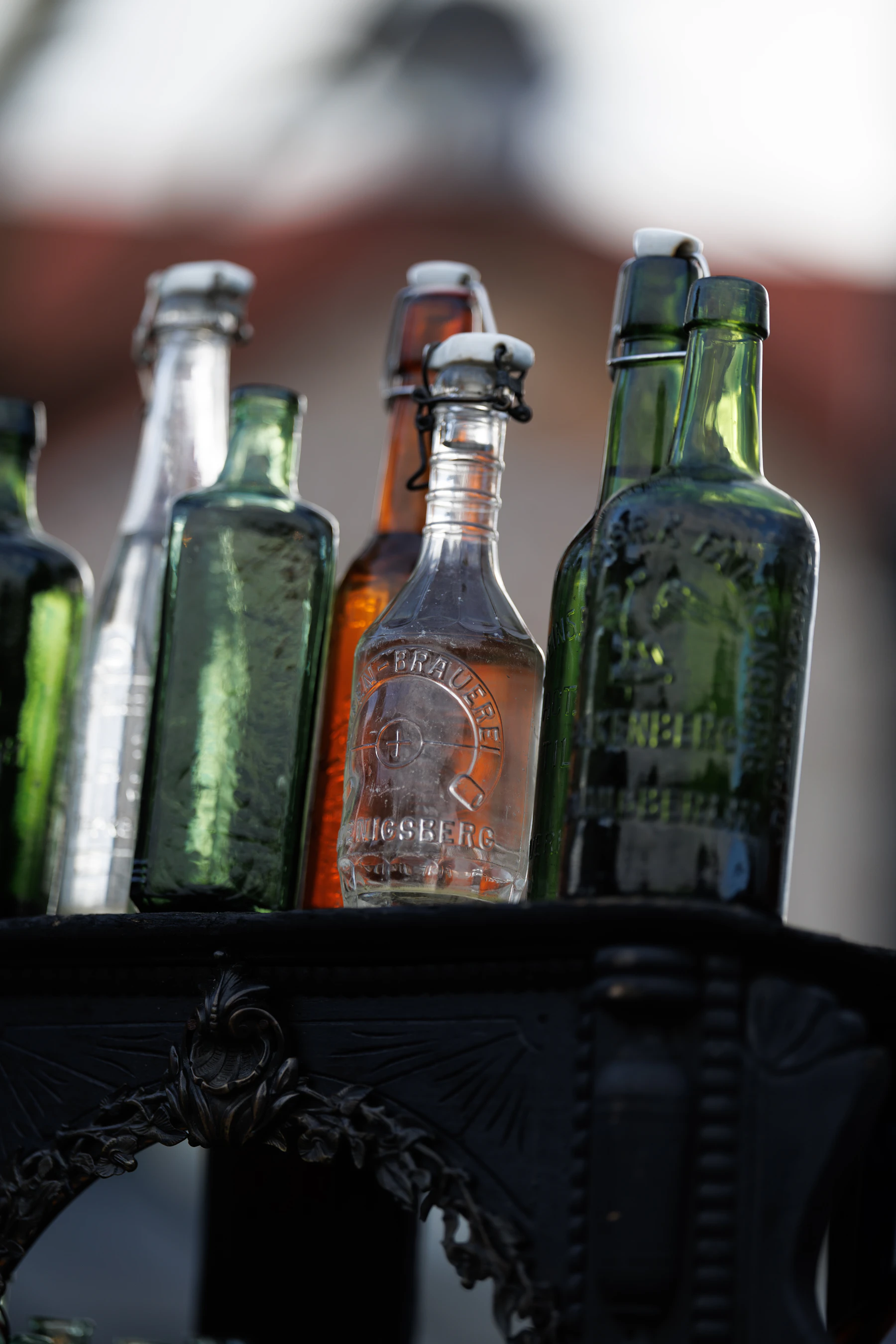 Embossed antique swing-top bottles in green, amber and clear glass standing on an iron stand