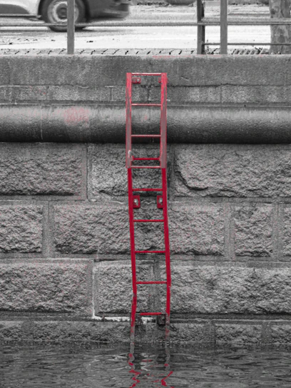 Red ladder partially submerged in water against stone wall
