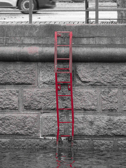 Red ladder partially submerged in water against stone wall