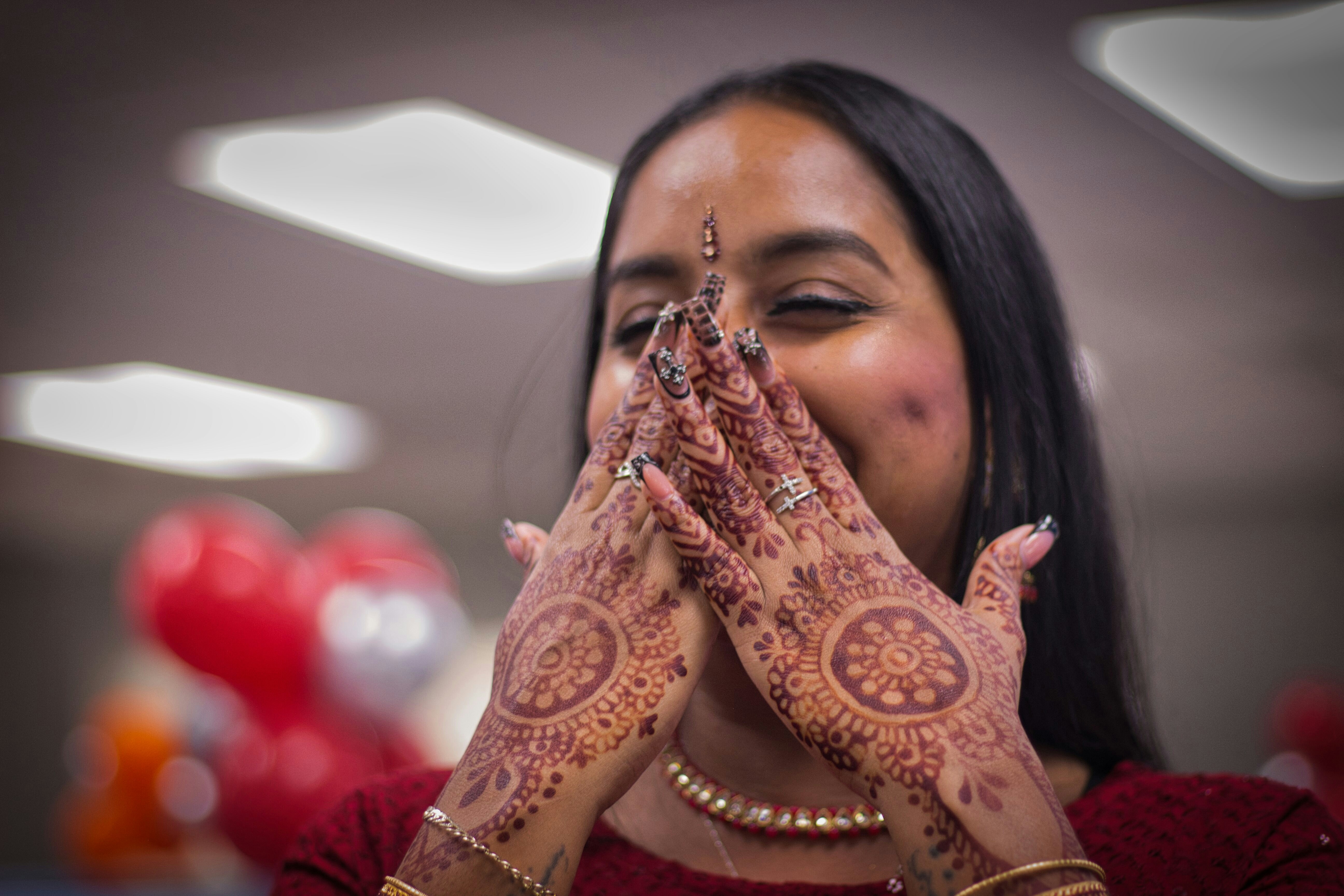 A joyful woman with intricate mehndi designs on her hands, smiling during a celebration in Trinidad and Tobago