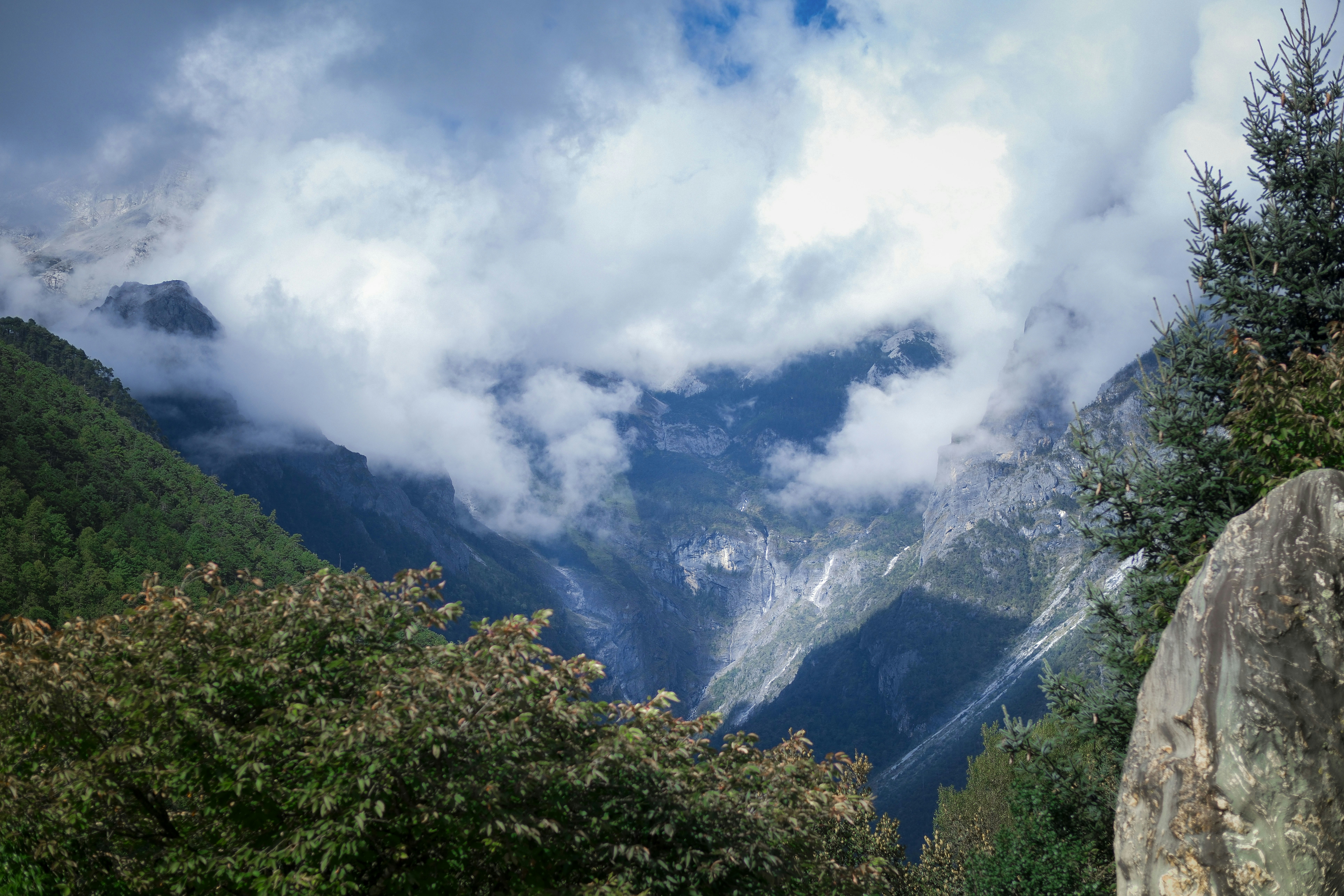 Misty clouds obscure a steep mountain valley with trees.