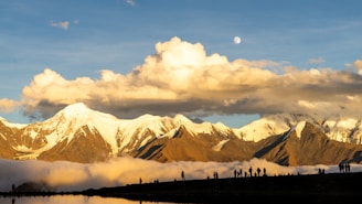 Snow-capped mountains under a cloudy sky with moon.