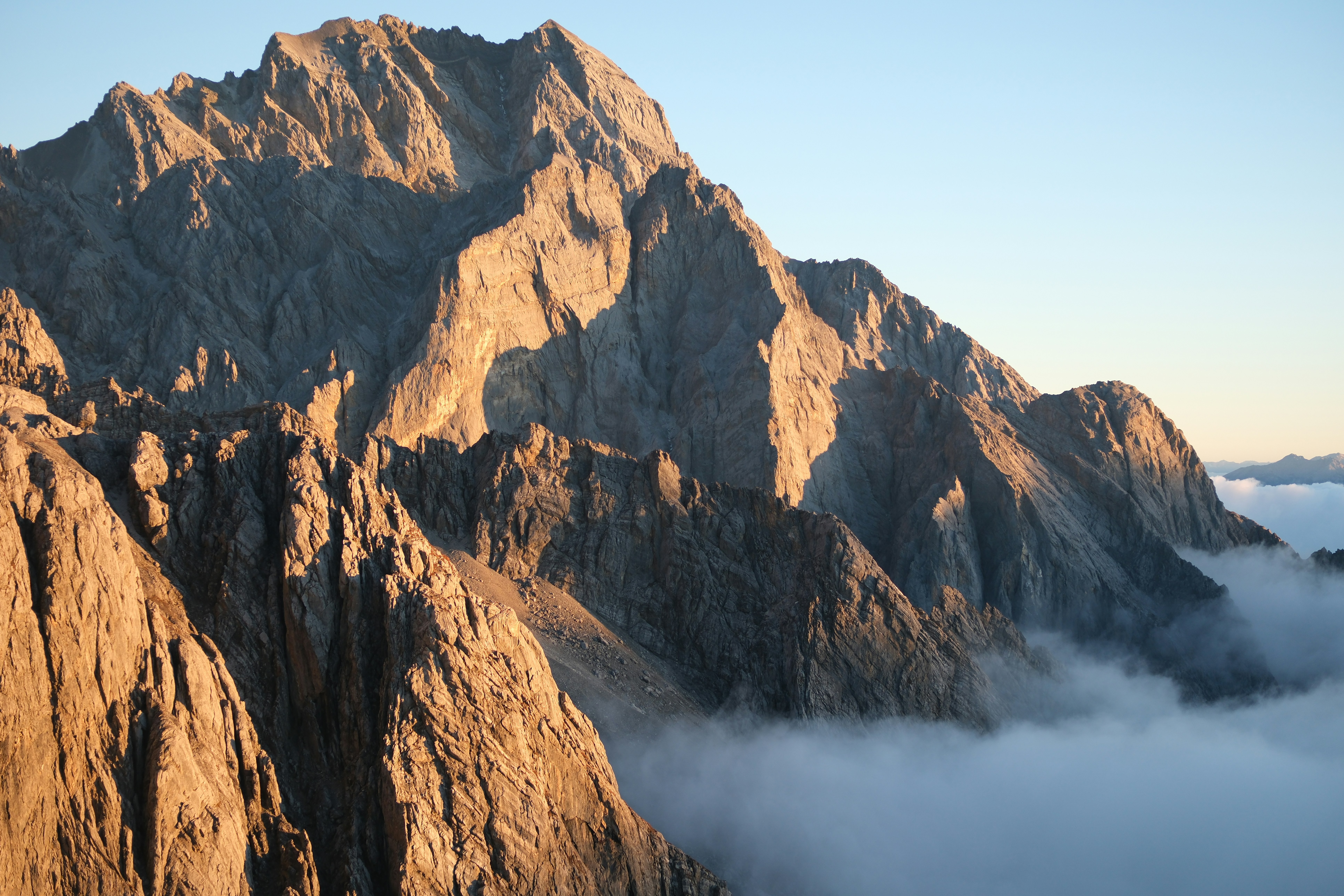 Jagged mountain peaks bathed in warm sunlight above clouds