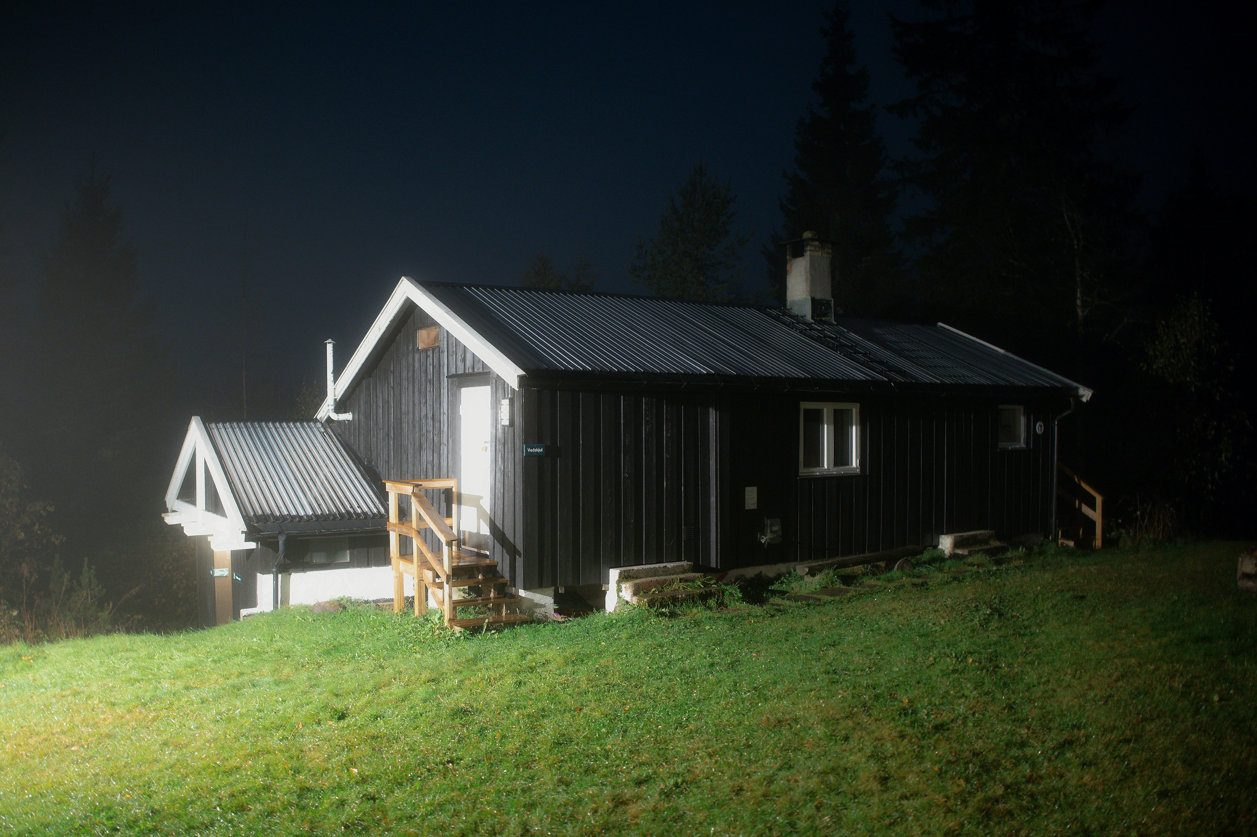 A dark wooden cabin on a grassy hill at night.