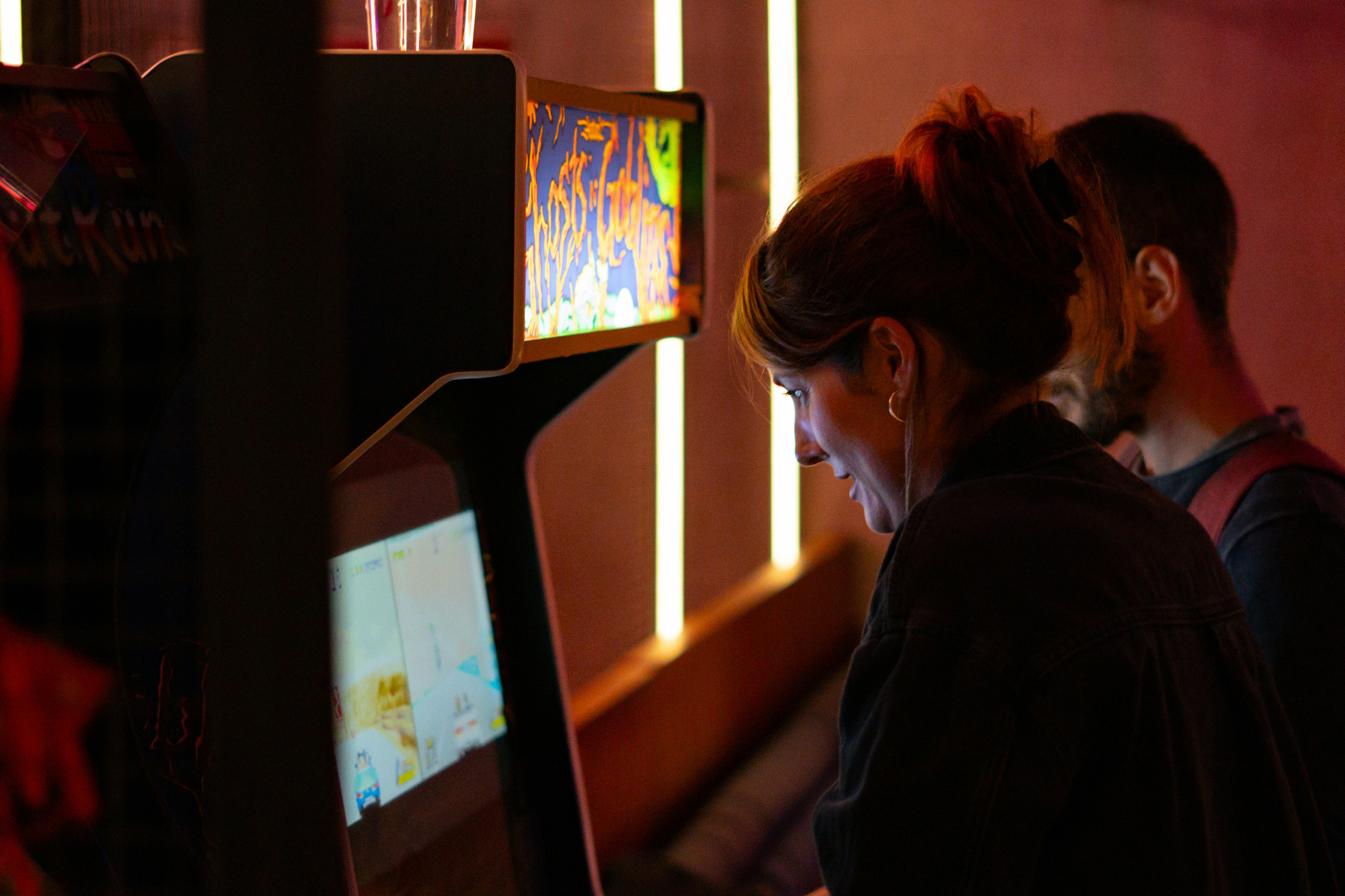 People playing arcade games in a dimly lit room.