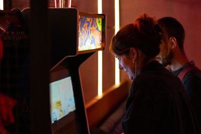 People playing arcade games in a dimly lit room.