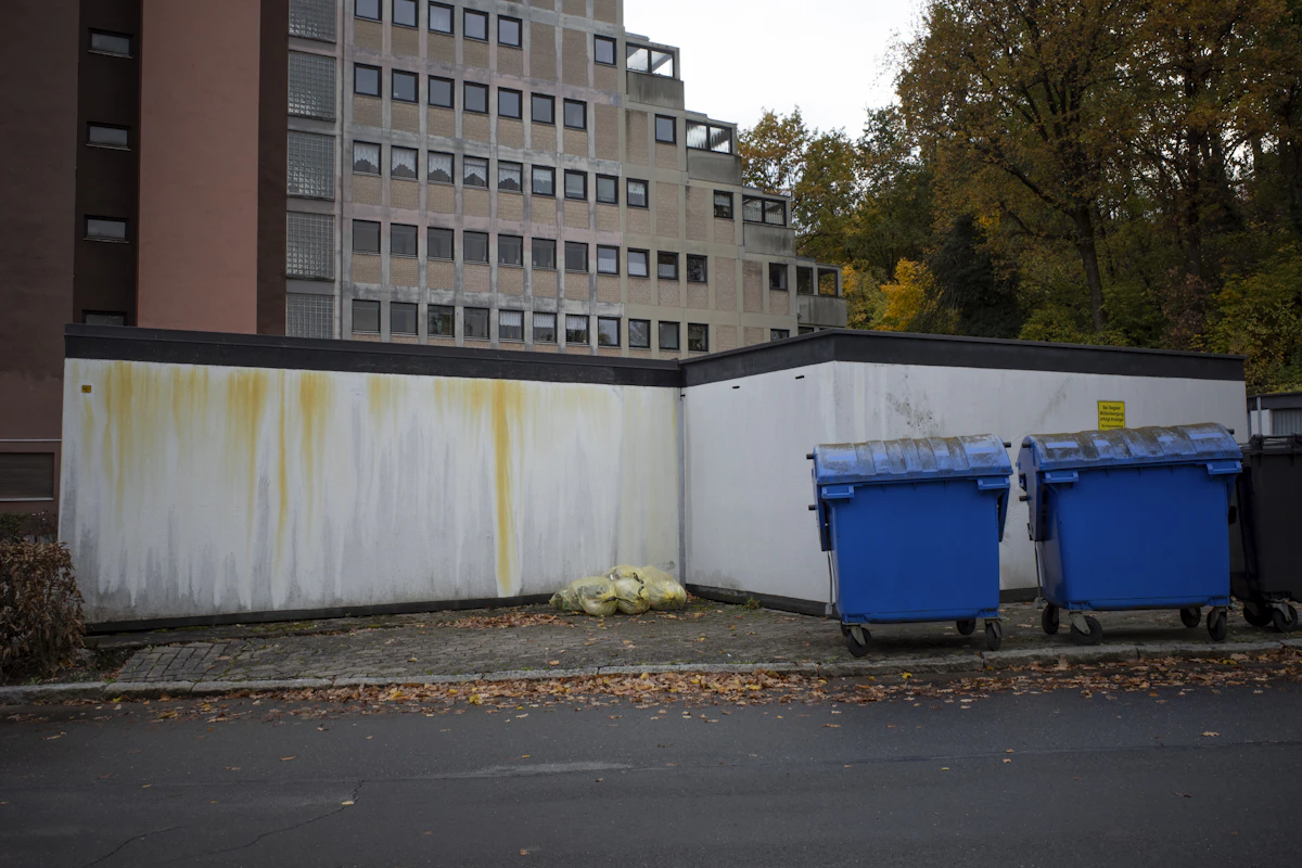 Two blue dumpsters next to an apartment building